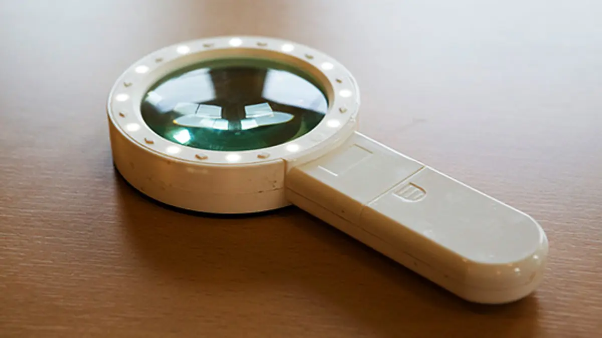 A white, illuminated handheld magnifier on a table.