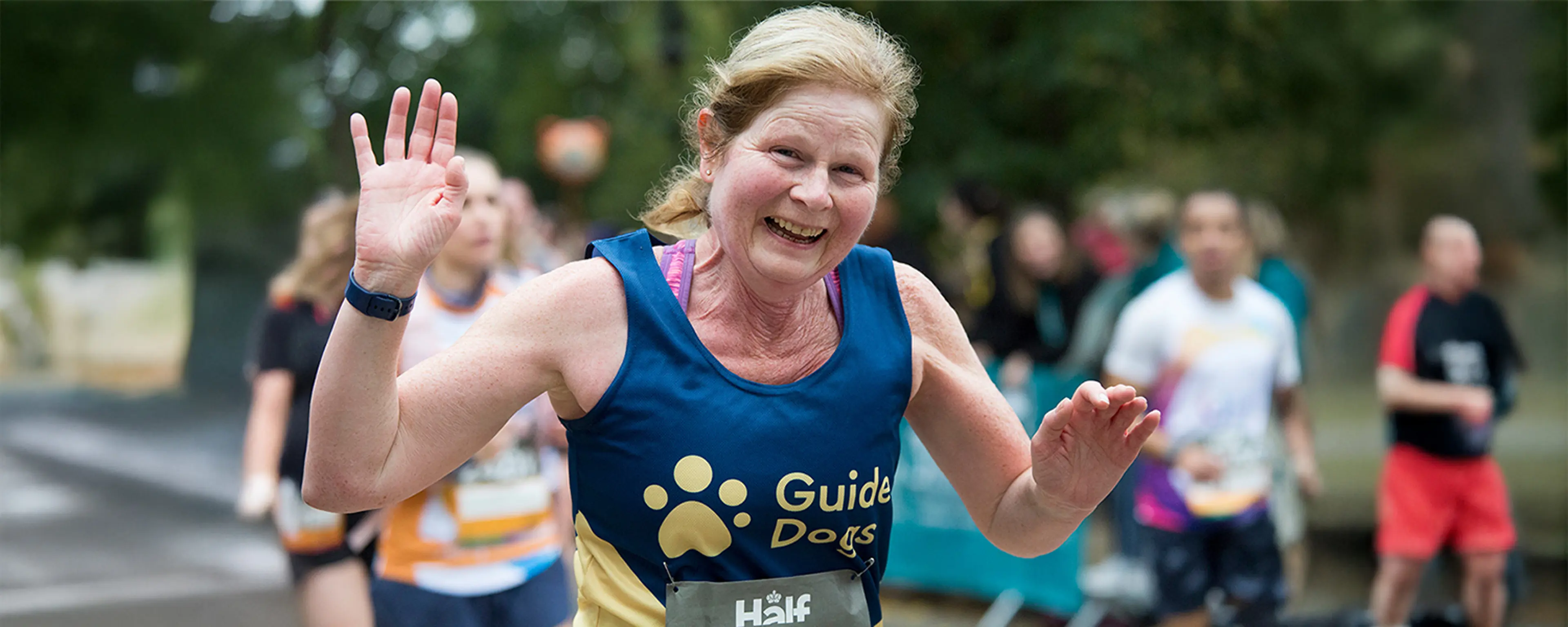 A marathon runner smiling and running in a Guide Dogs vest.