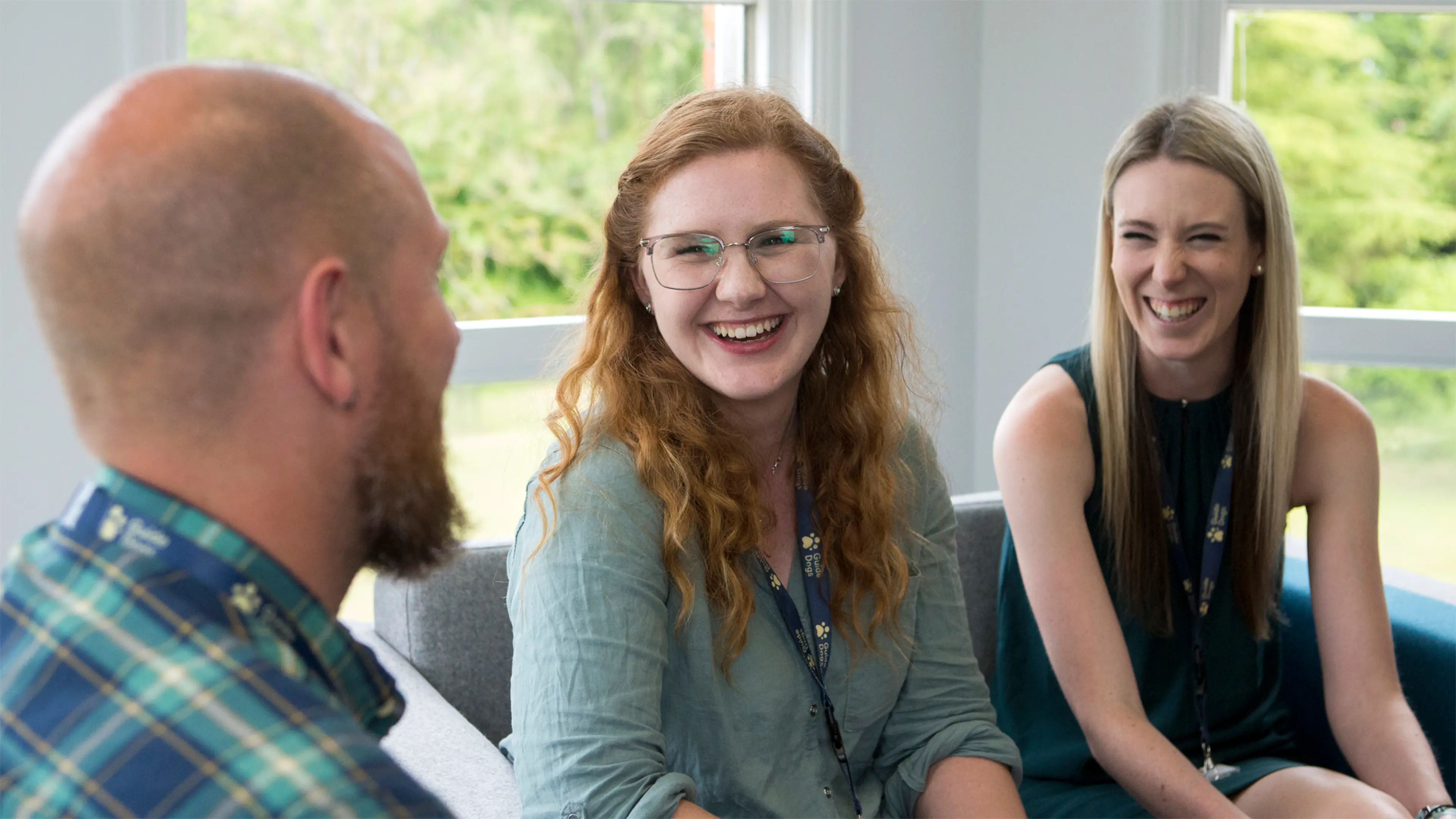 Three Guide Dogs colleagues laugh and smile as they sit by a window in the Reading office.