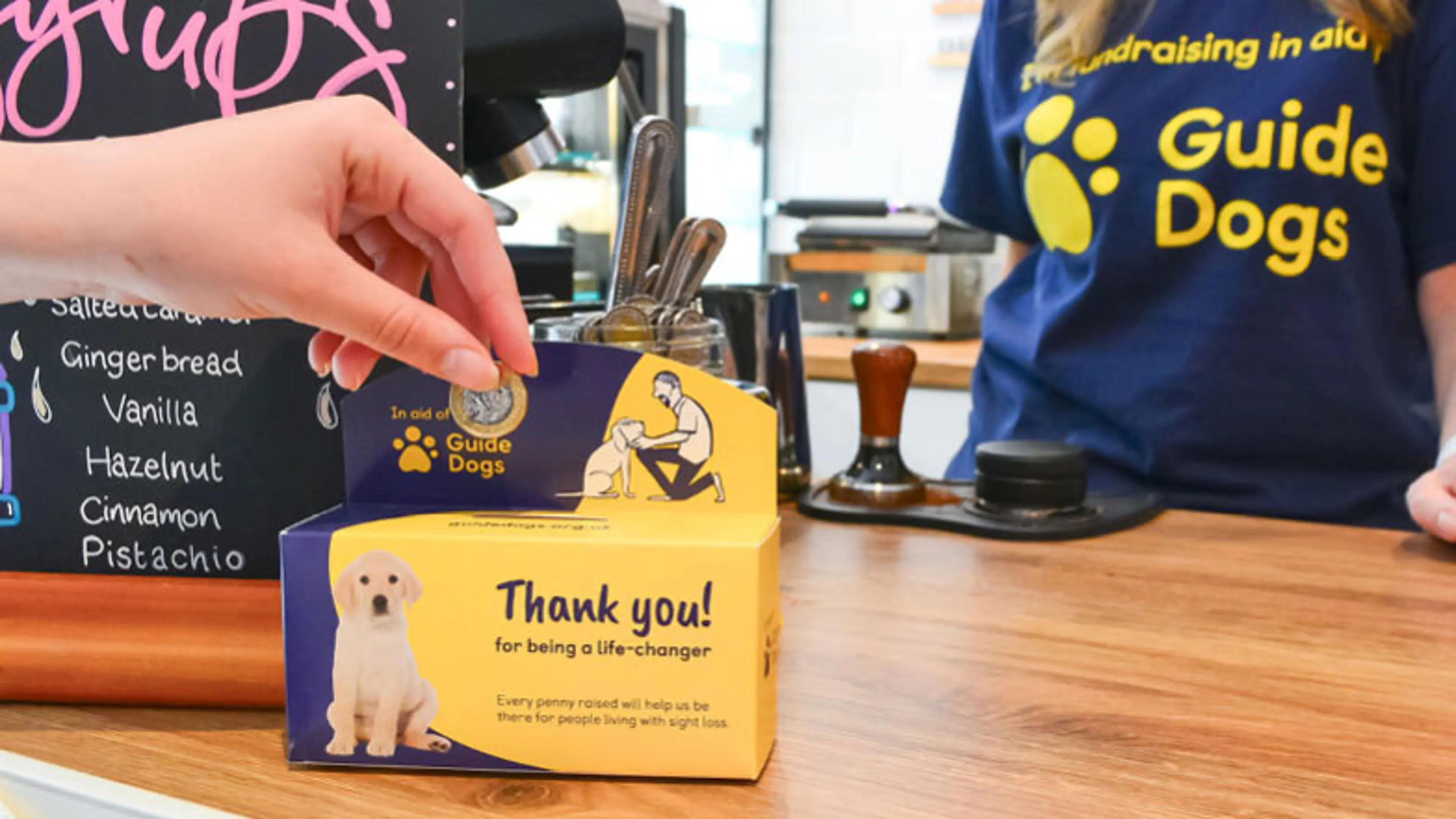 A close-up of someone's hand holding coins donating to a Guide Dogs coin collector 