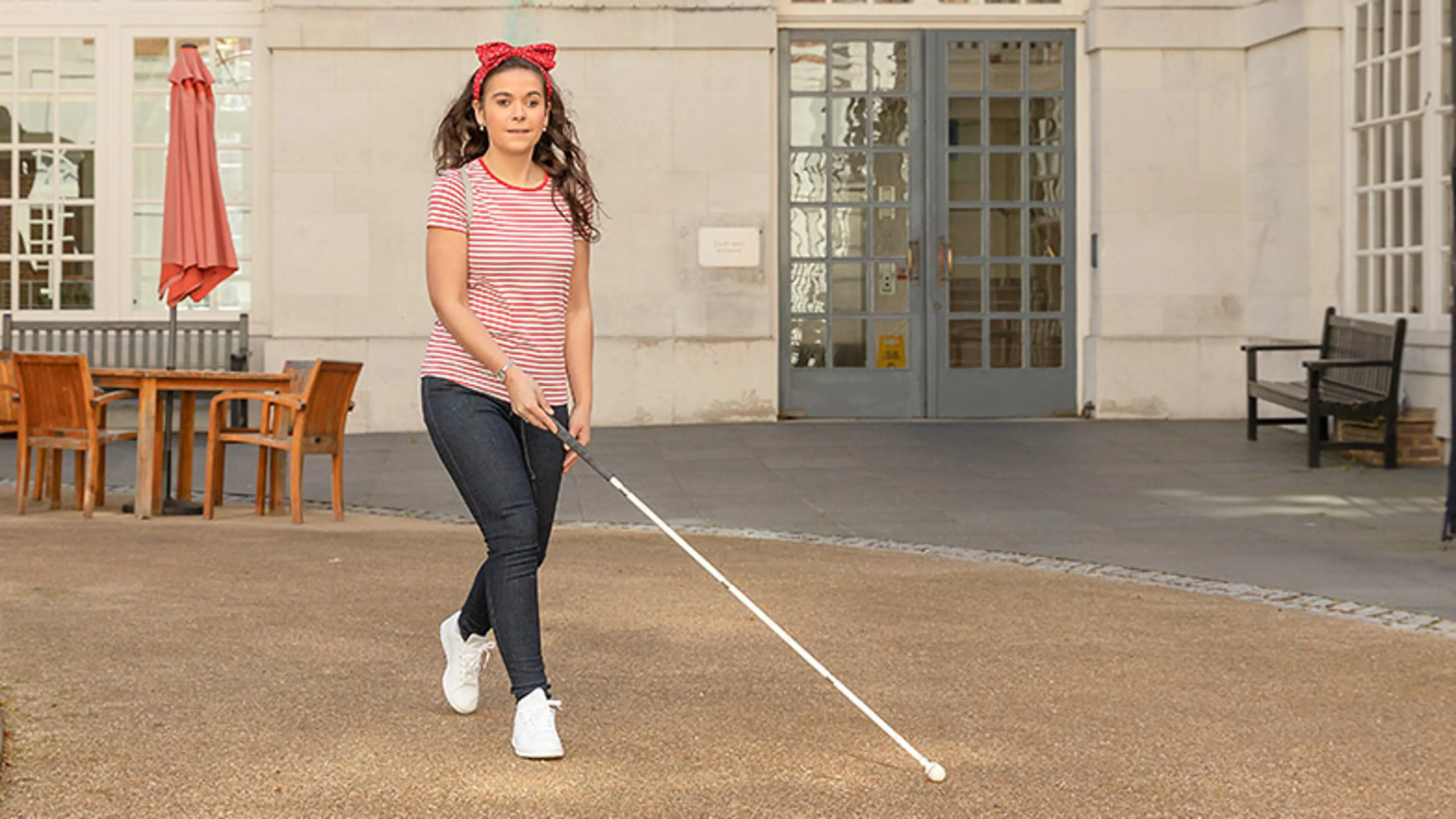 A woman using her long cane outside to navigate across a courtyard.
