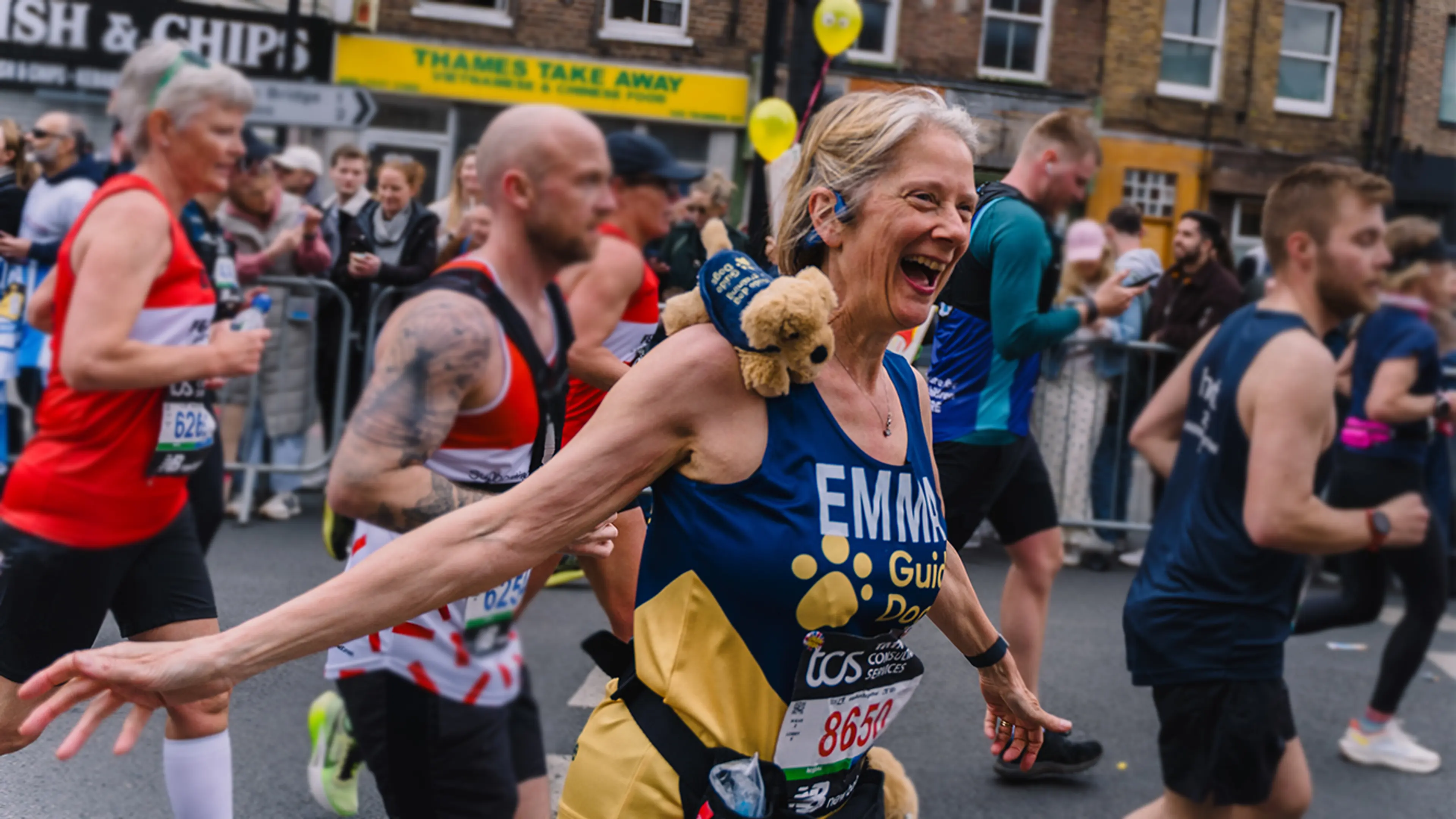 Emma running the London Marathon for Guide Dogs with a small guide dog puppy toy on her shoulder.