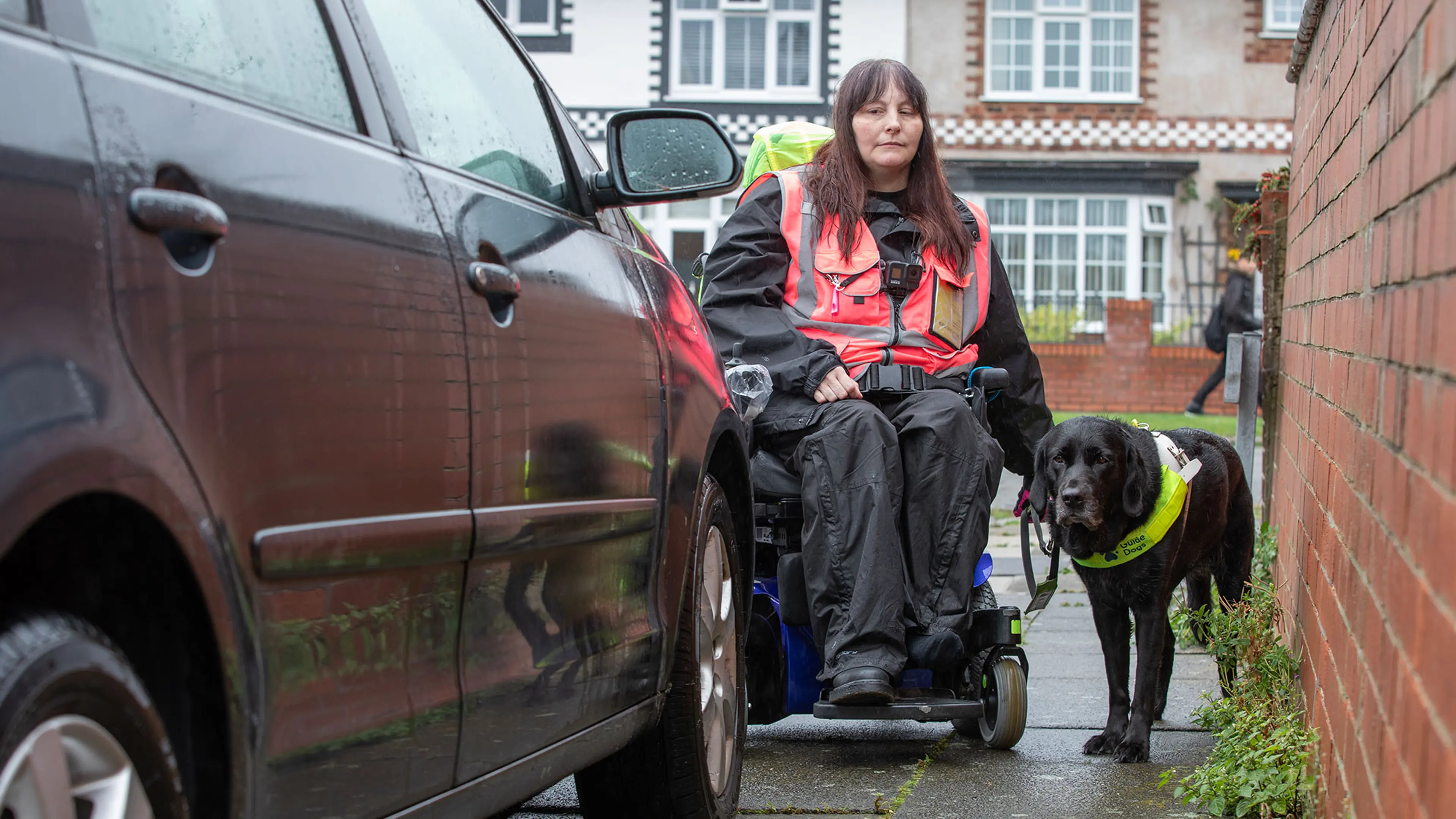 Guide dog owner Julie with guide dog Maeve trying to pass through a gap to avoid a car parked on the pavement.