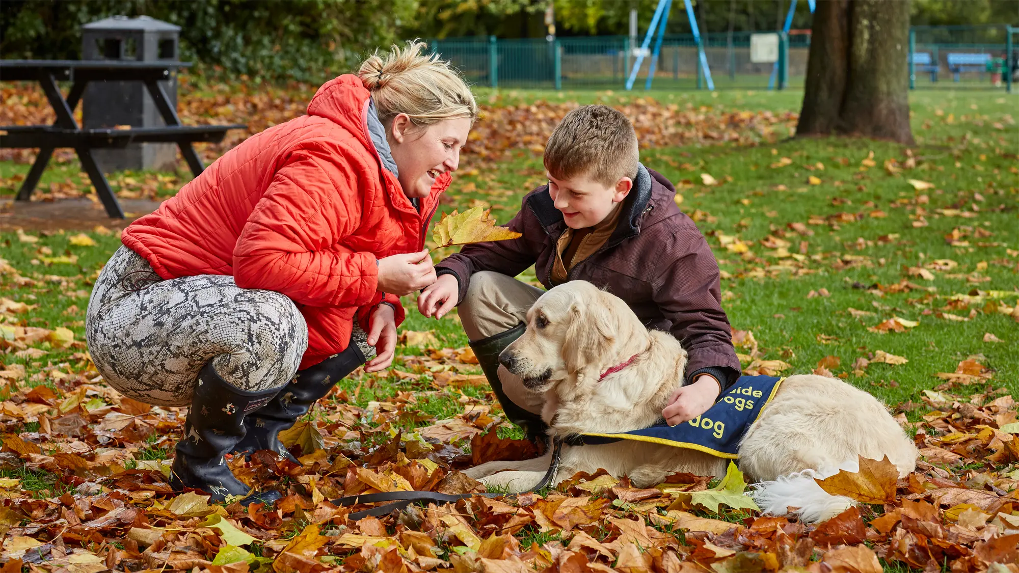 Archer, who has a vision impairment, crouches down in colourful autumn leaves with his mum and buddy dog Nancy.