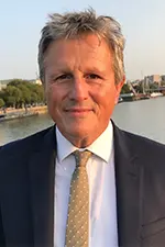 Mark smiles at the camera. He has short grey hair and is wearing a black suit with a gold tie.