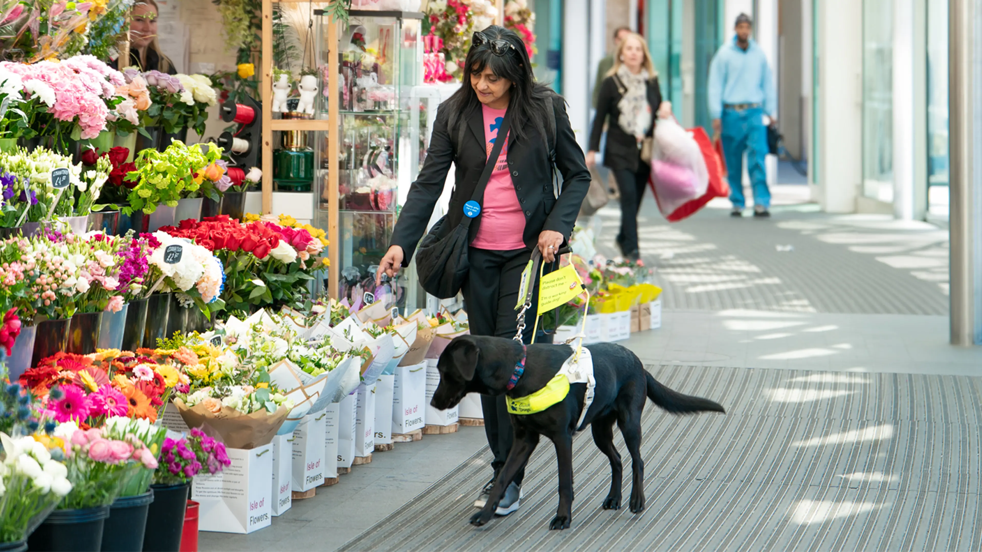Deborah and her black Labrador guide dog Betty walk through a station together past a flower stall.
