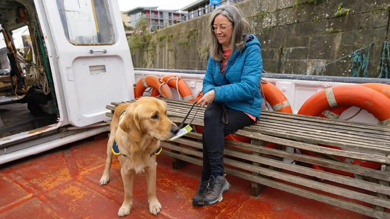 Puppy Raiser Vicky sitting outside on a boat with Walter standing in front of her.
