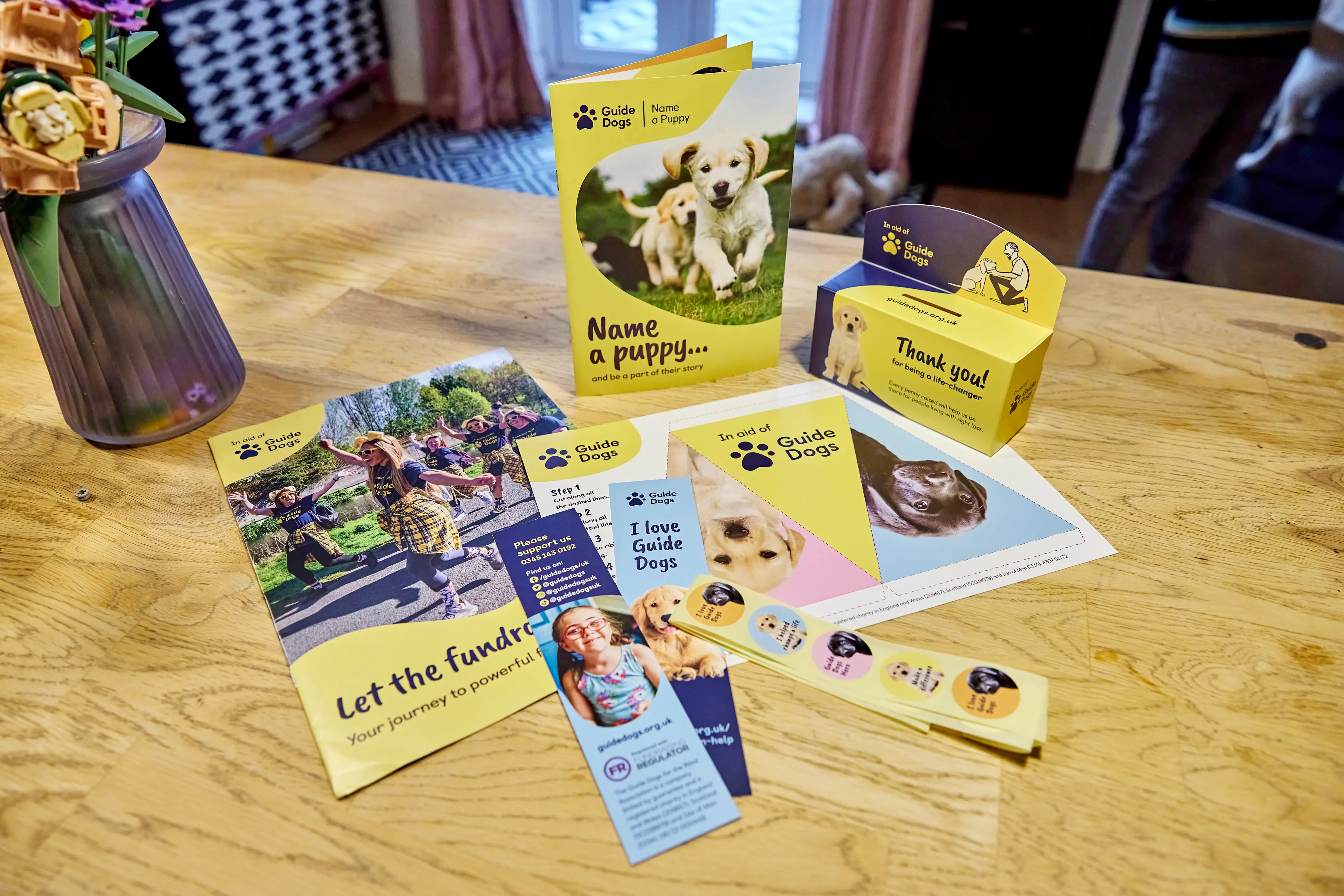 Table with Guide Dogs' fundraising items on, including leaflets and a collection box.
