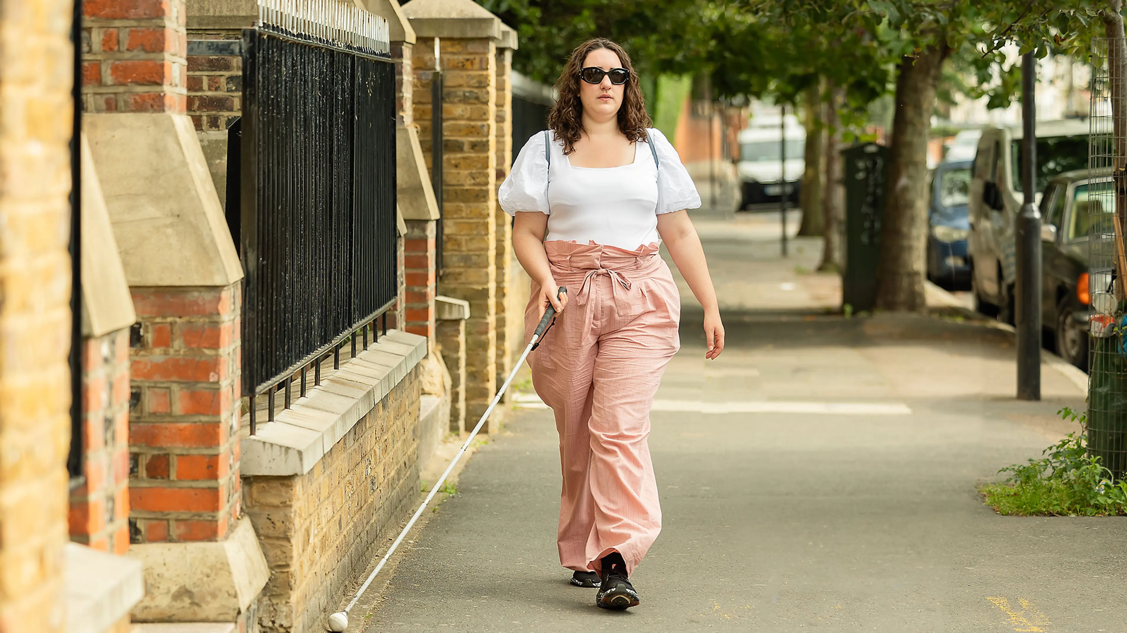 Long cane user Cerys walking along a pavement.
