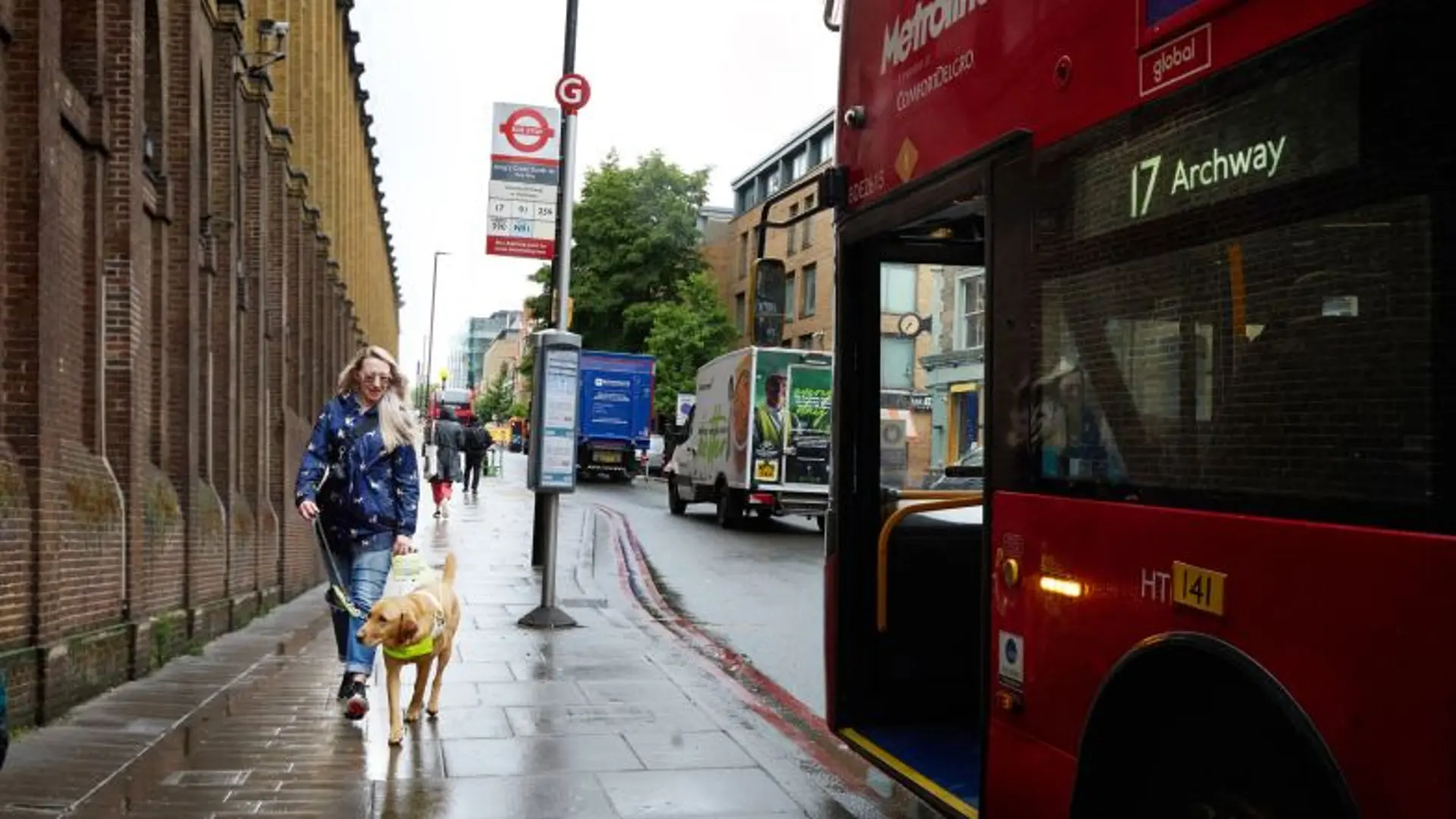 Guide dog owner Emma walks with her guide dog Archie past a bus stop on a London street.