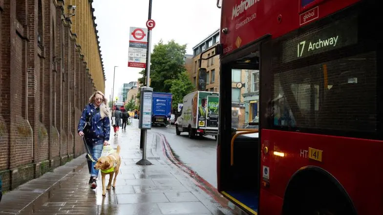 Guide dog owner Emma walks with her guide dog Archie past a bus stop on a London street.