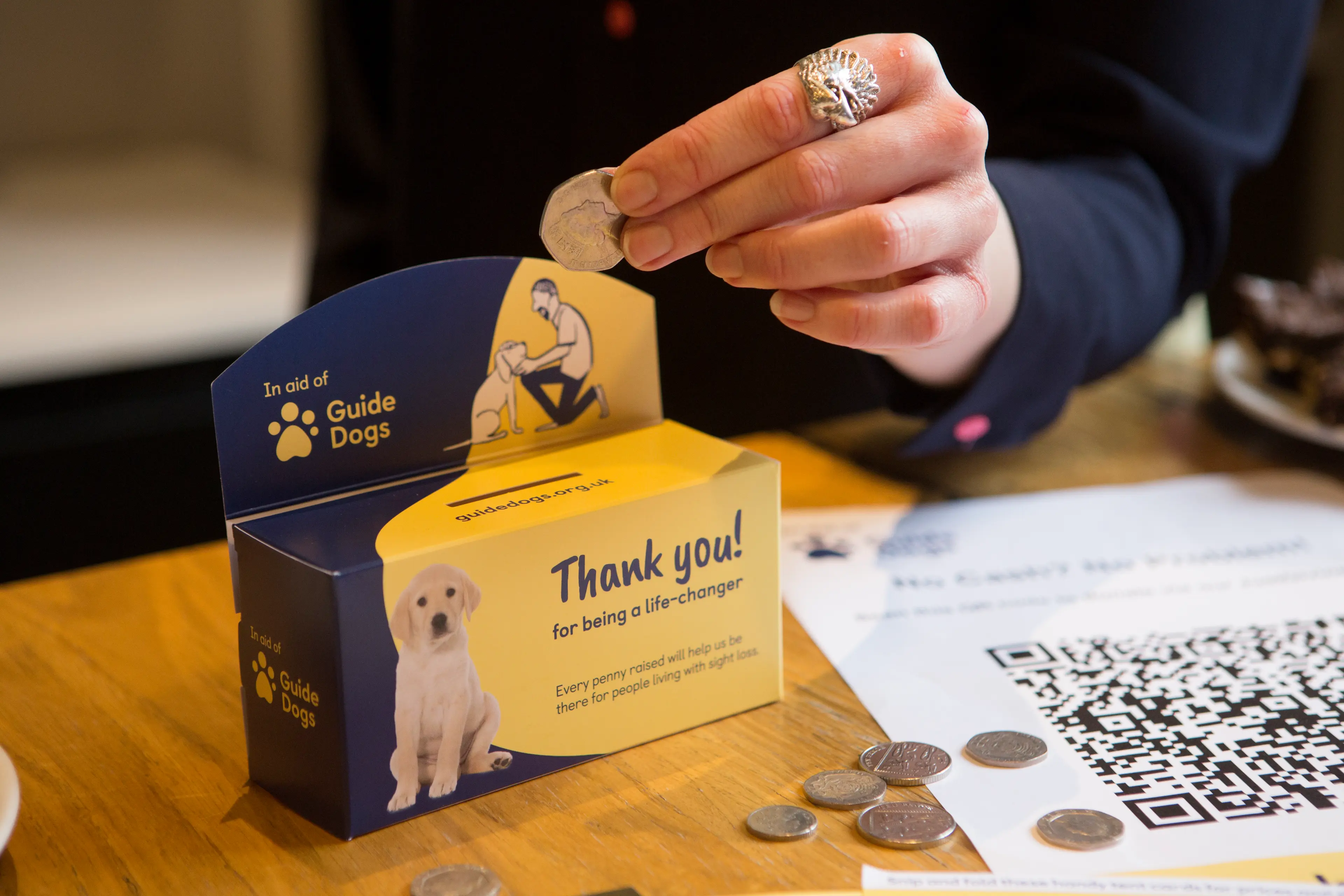 A person puts 50p into a Guide Dogs collection box.