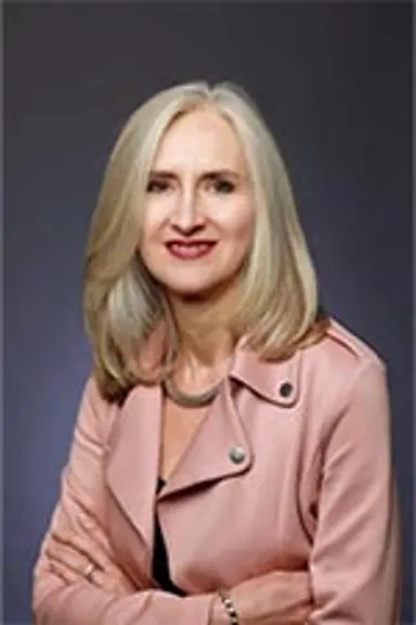 Helen smiles at the camera. She has long blonde hair and is wearing a light pink jacket.