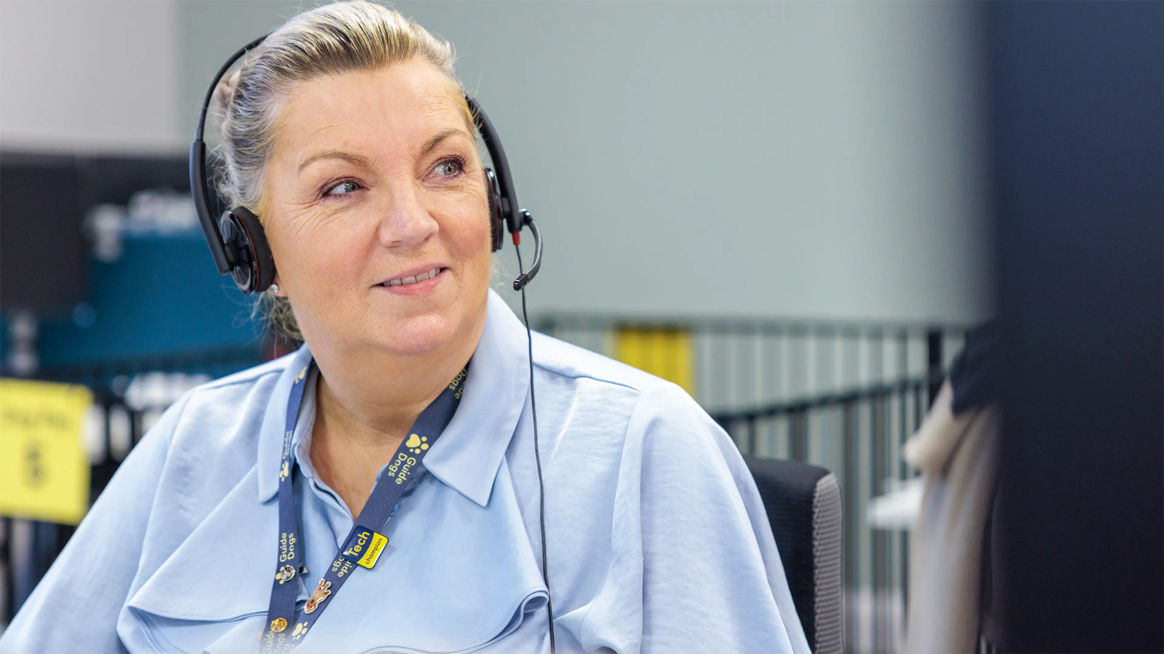 A Guide Dogs employee looks up from her desk, she wears a headset to take phone calls. 