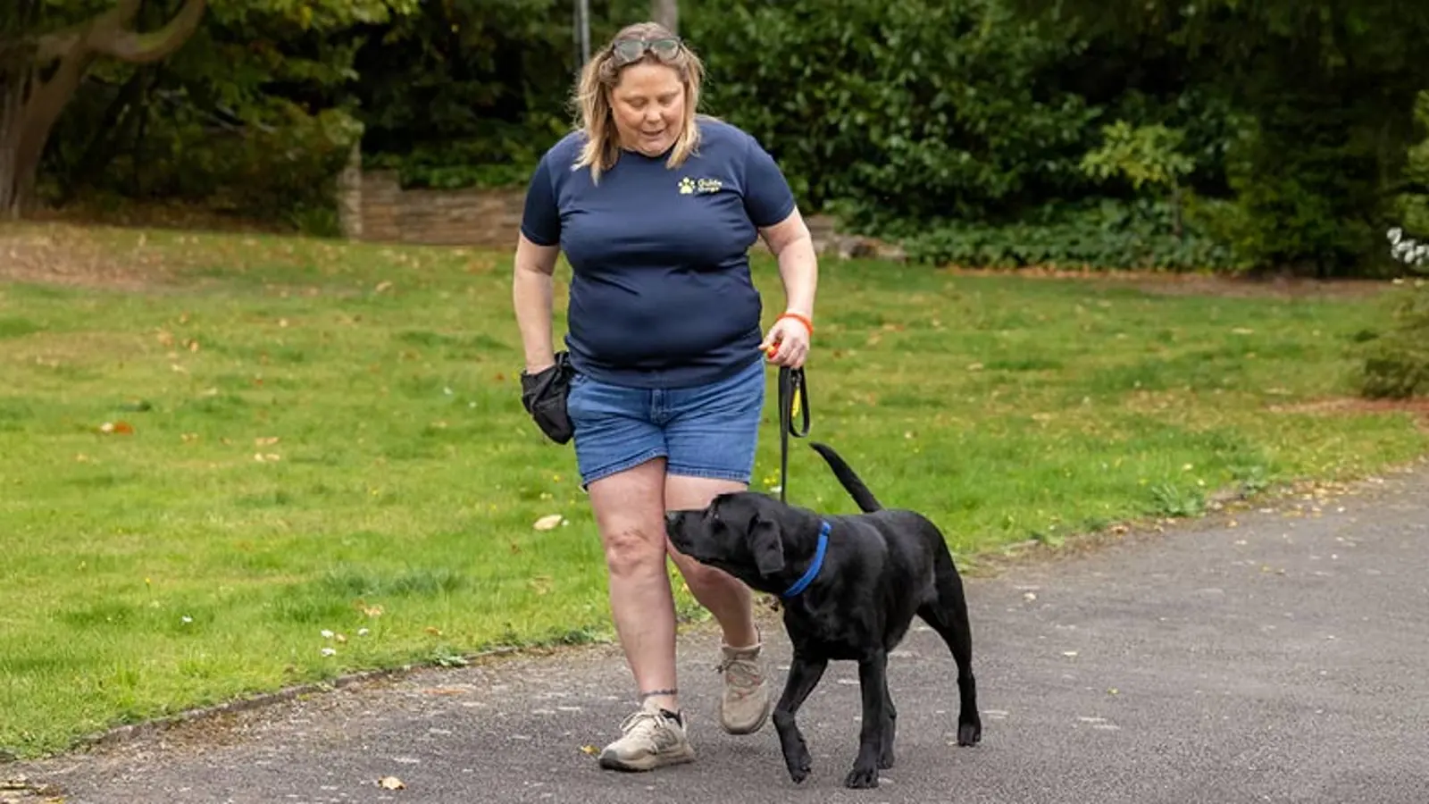 Rachel and Jack walking in a park. Rachel has her hand in a treat bag.
