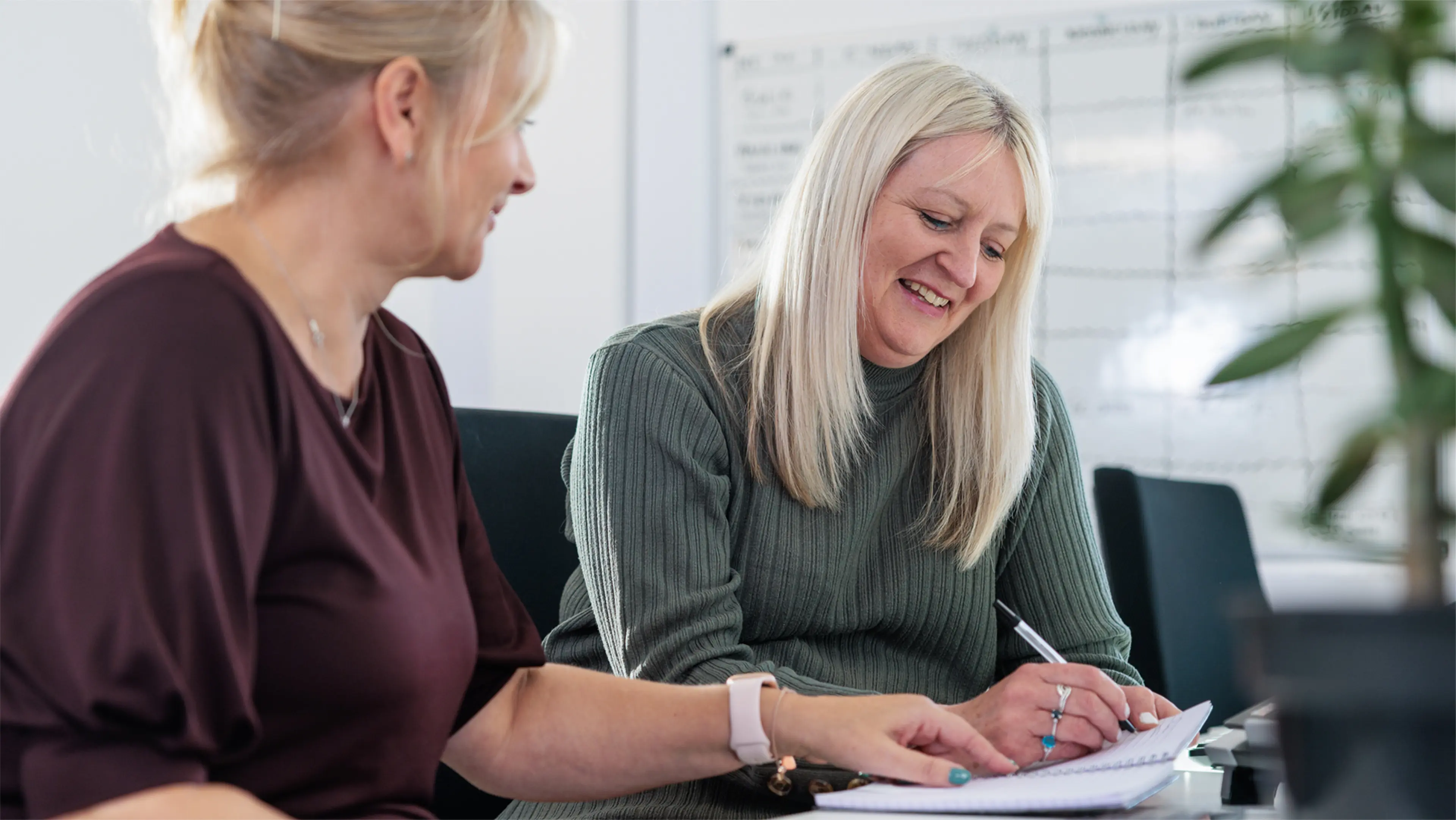 Two Community Fundraising team colleagues work side by side at a desk, one of them takes notes. 