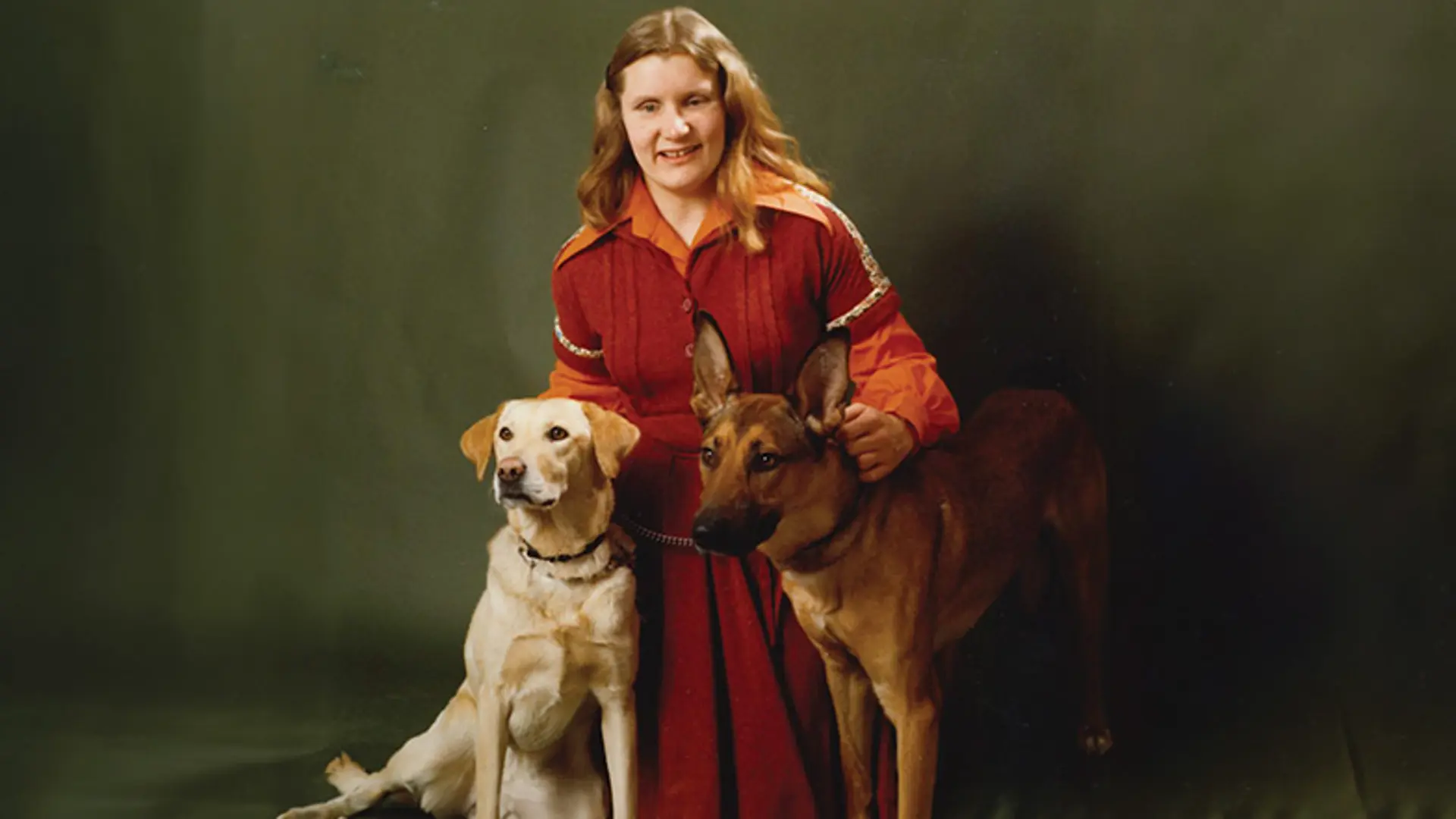Danni standing with 2 dogs by her side, a Labrador and German shepherd.