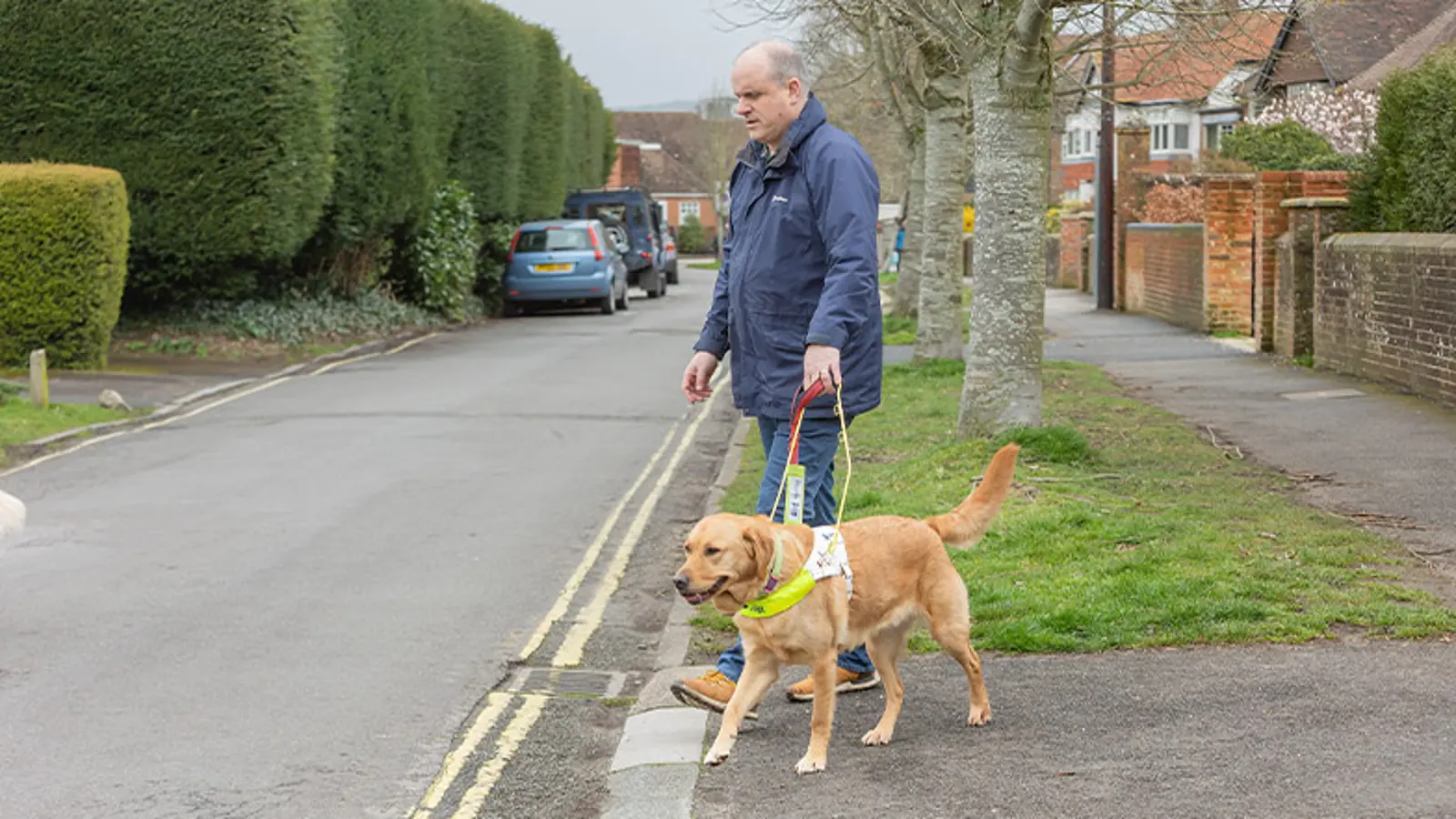 A guide dog owner approaches a drop kerb with his guide dog