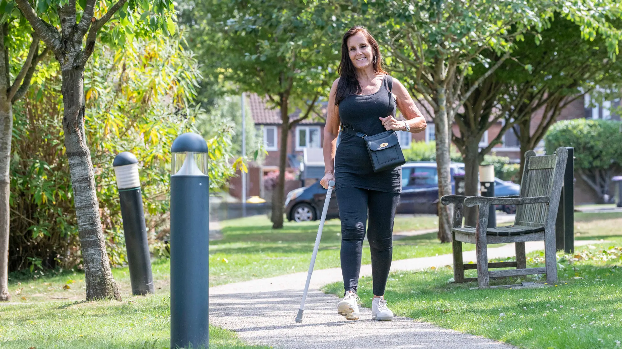 Jennie, who has a vision impairment, walks along a path in a sunny park.