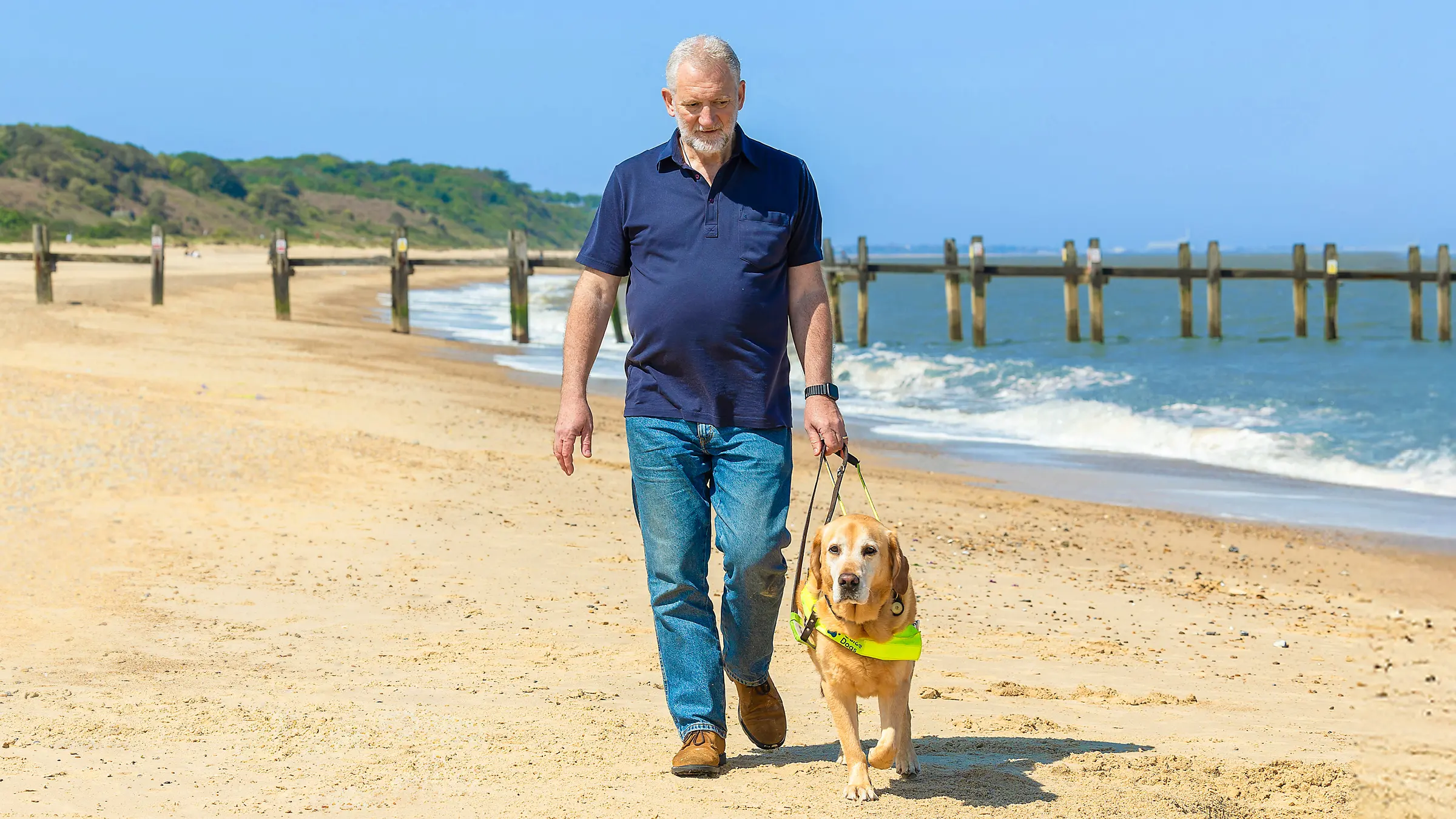 Guide Dog owner Simon walks along a beach with his guide dog Mayne.