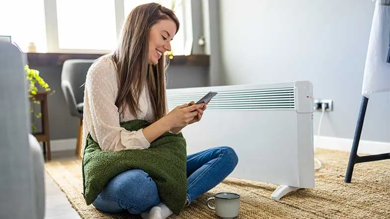 A woman sitting on the floor controlling  a portable smart heater with her phone.