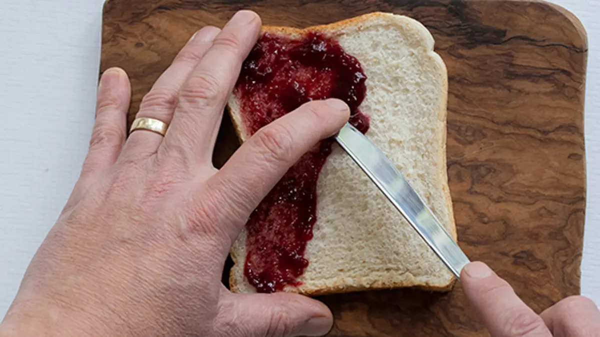 Someone using the bridge technique to spread jam onto a piece of bread. 