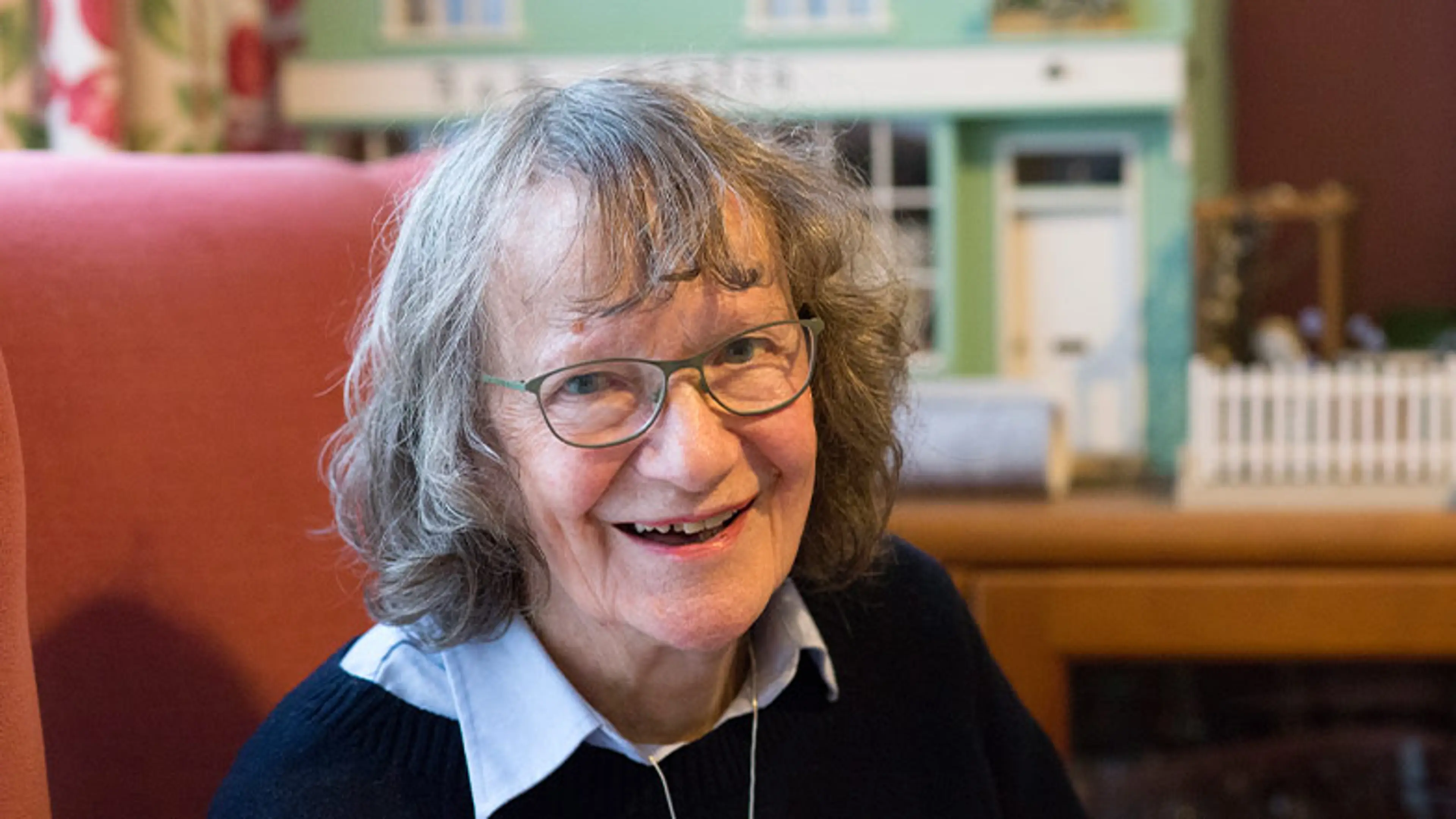 Hilary smiles to camera while sitting in an armchair.