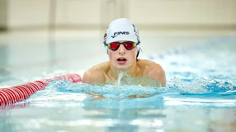 Archie swims toward the camera. He is wearing a swimming cap and goggles.