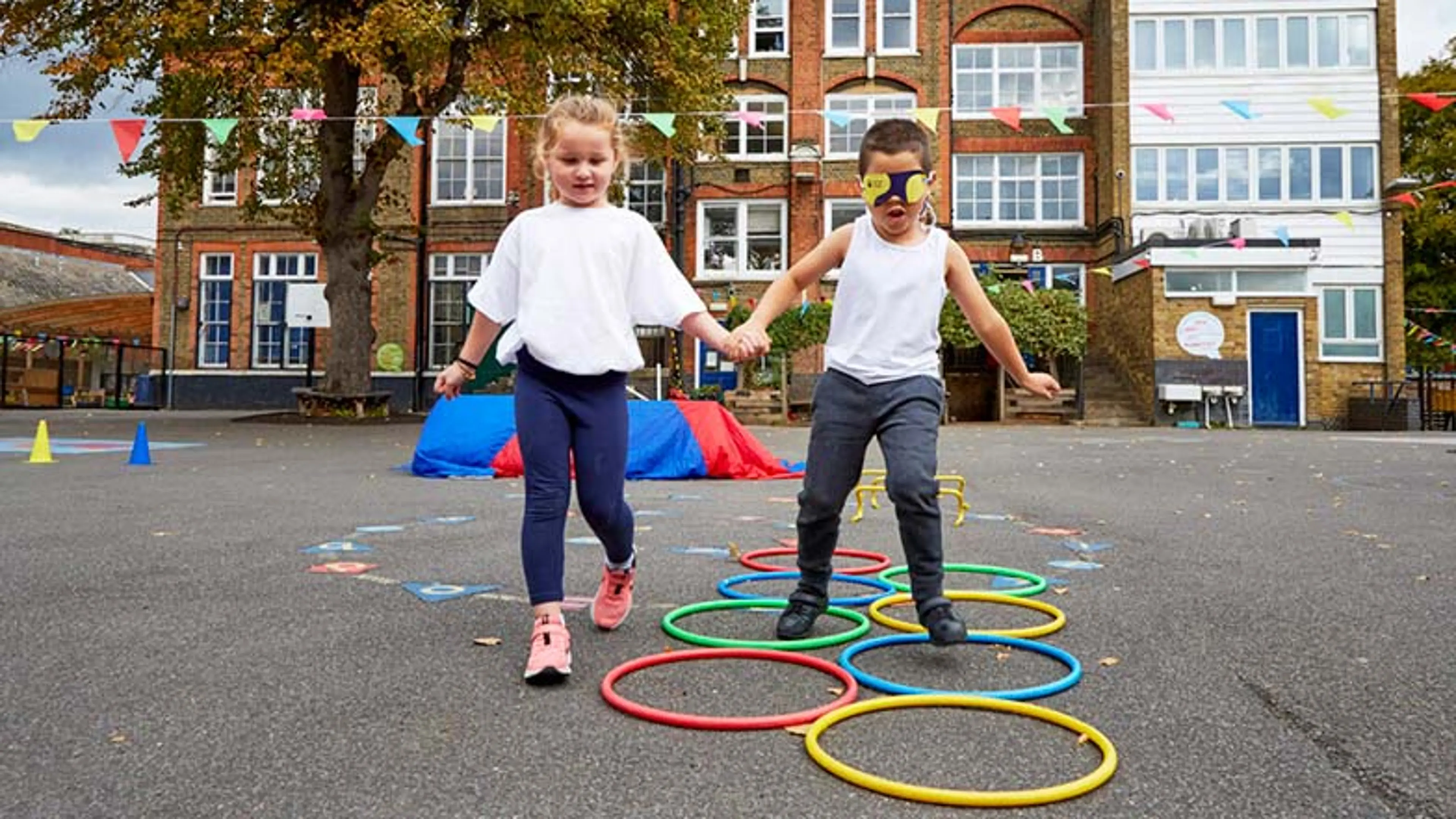 Two schoolchildren doing an obstacle race, one blindfolded and one holding their hand to guide them.