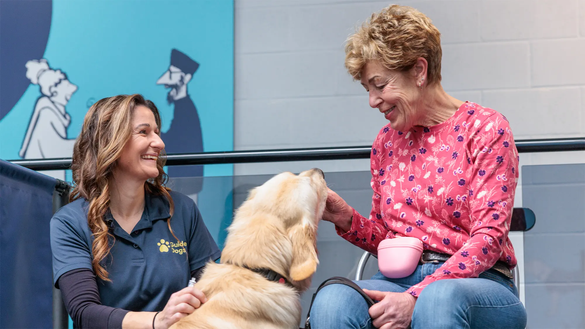 A Puppy Development Advisor and a volunteer Puppy Raiser smile as they work on training techniques with a golden retriever guide dog puppy. 