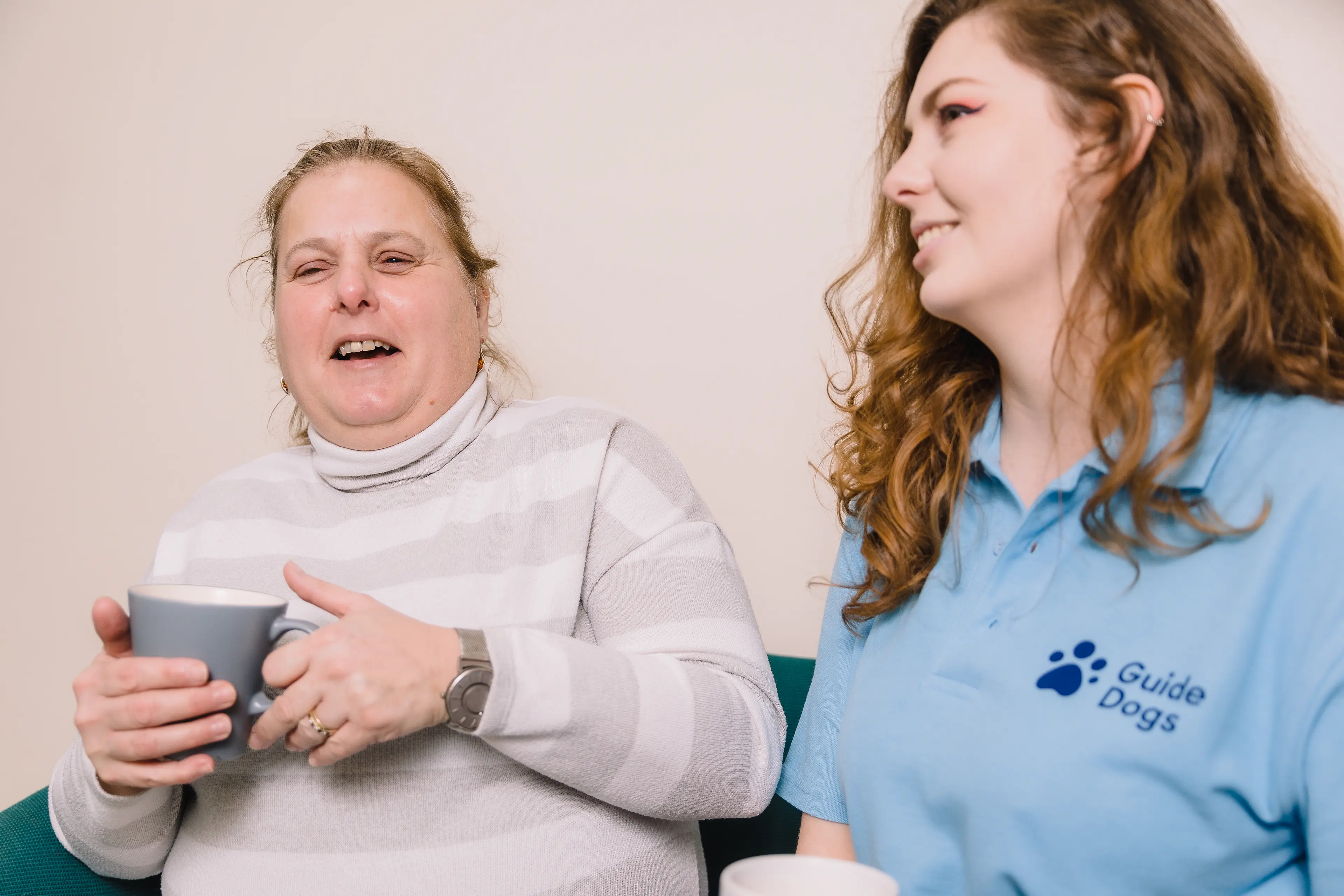 Two women sit side by side laughing.