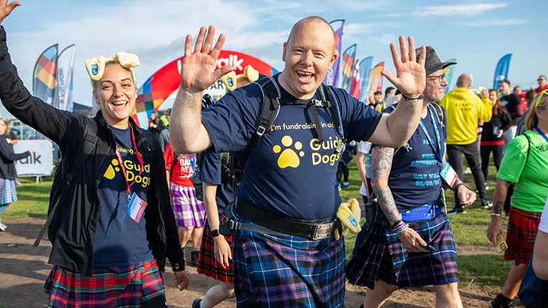 People pictured smiling wearing Guide Dogs fundraising t-shirts walking a Kiltwalk route.