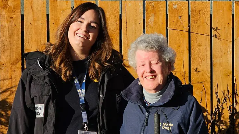Margaret smiles in the sunshine next to her Visual Rehabilitation Specialist.