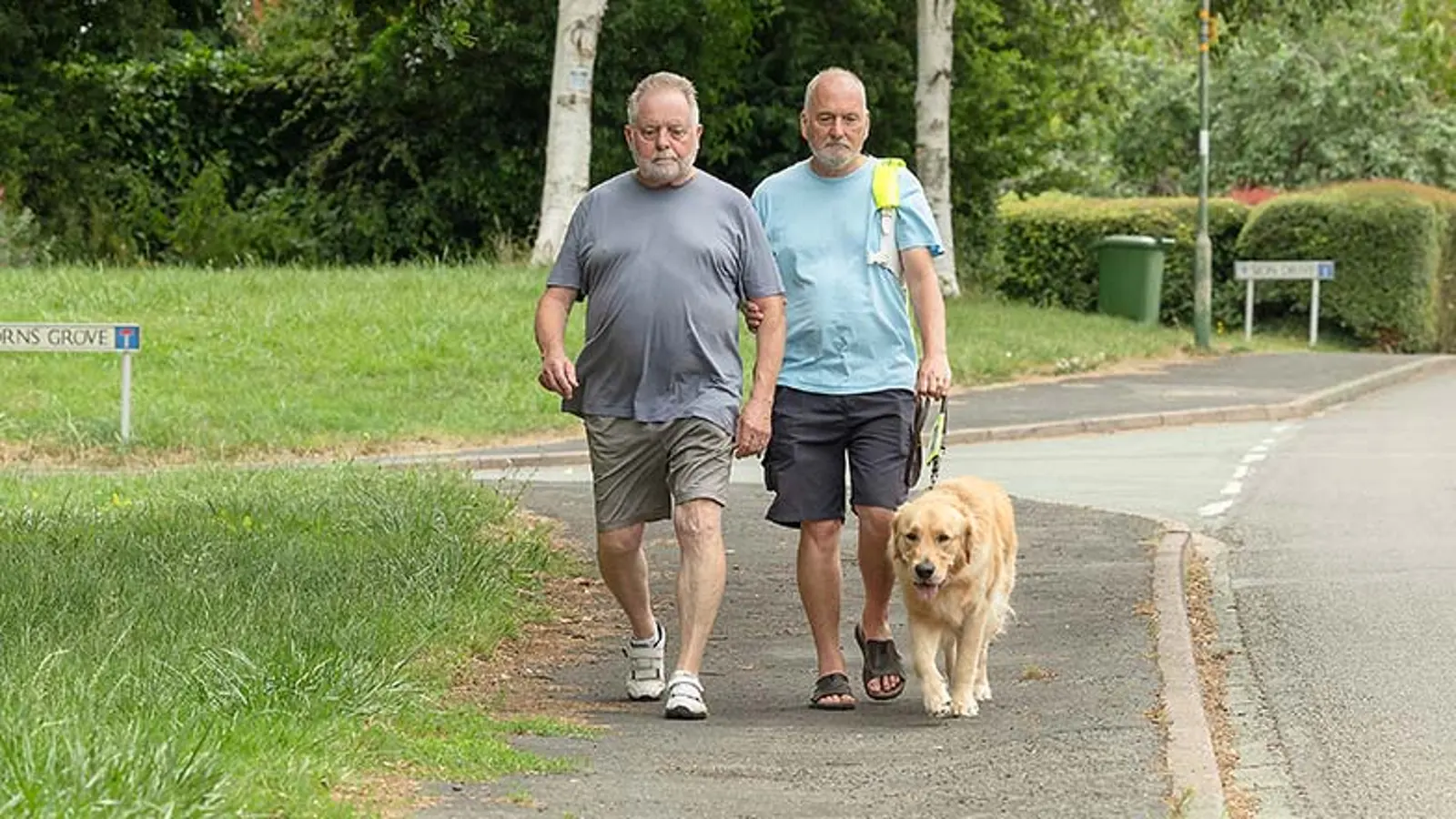 A guide dog owner practises a new route with his guide dog. His partner walks beside them.