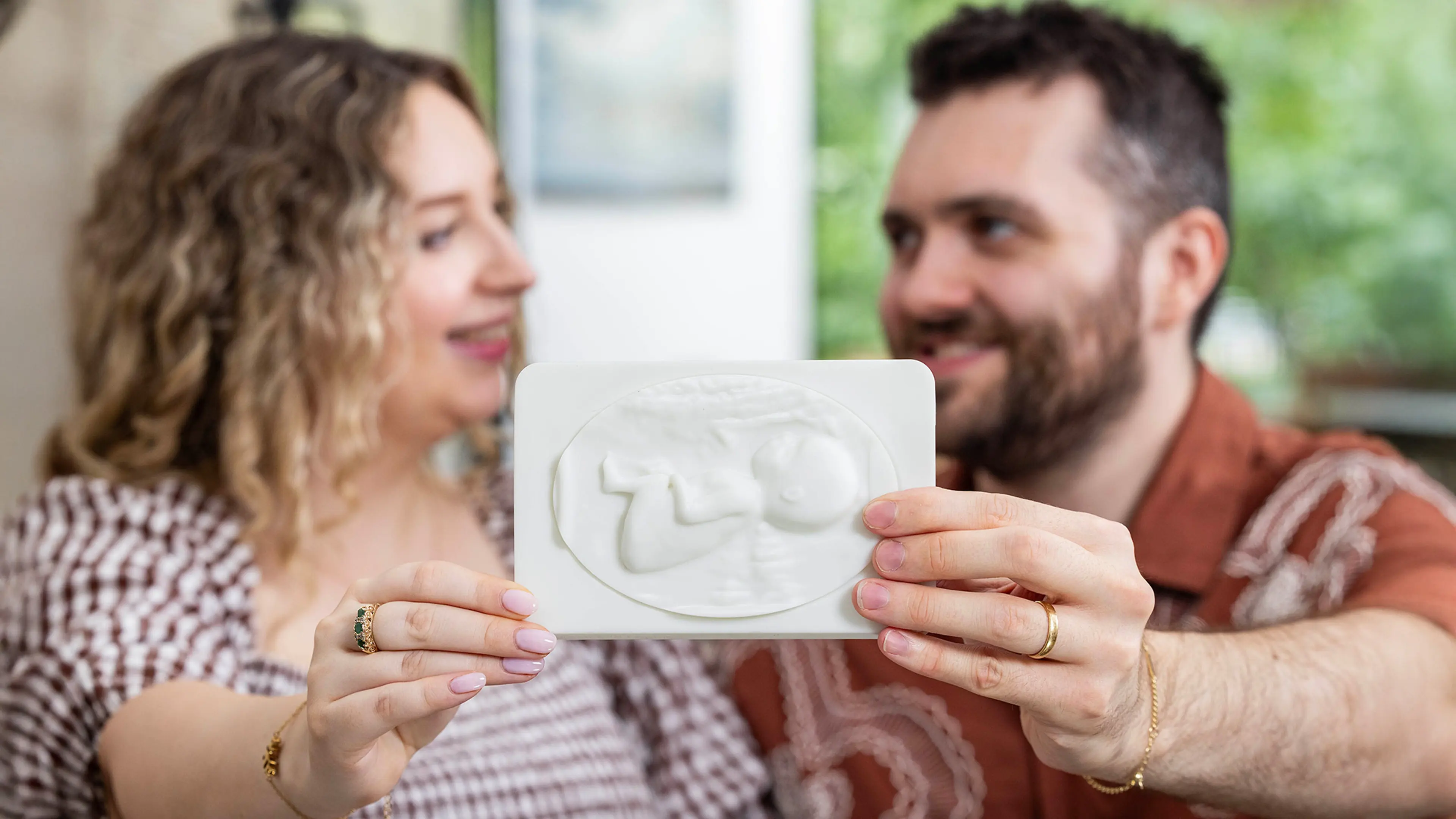 Sophy and Reece both hold their First Hello tactile sonogram up to the camera in front of him them.