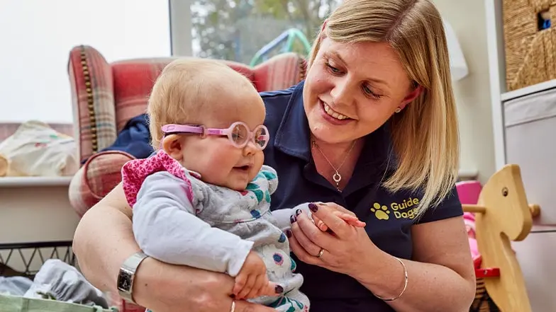 A Habilitation Specialist smiles as she plays with a young service user.