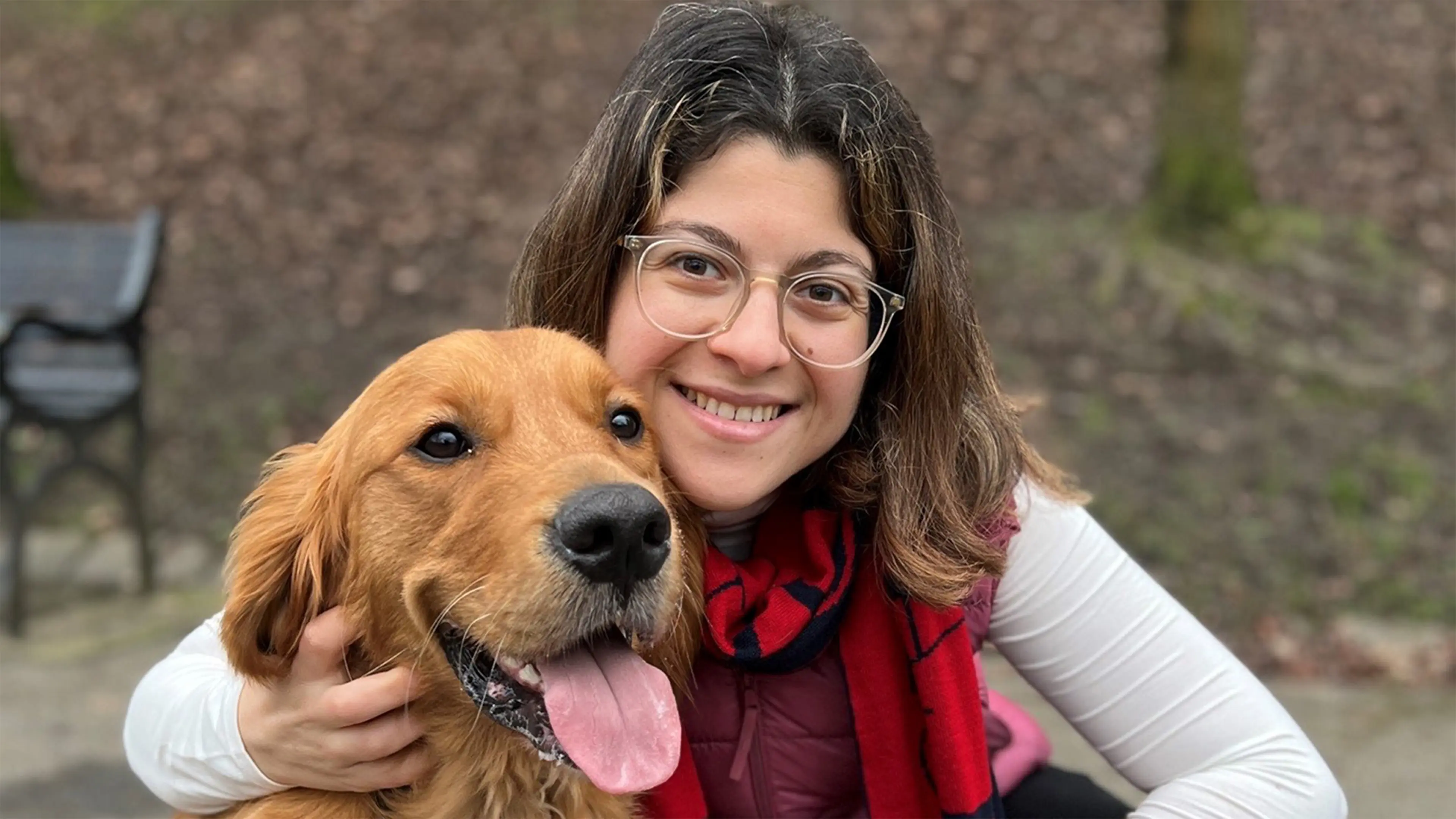 Guide dog owner Zee smiles to camera in a park, with her arm around her guide dog Mitch.