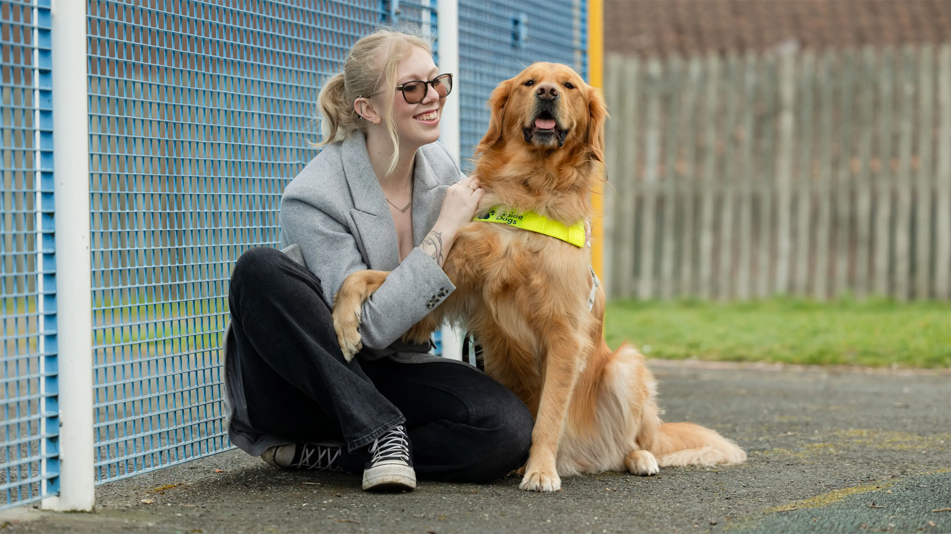 Hannah sits in a playground smiling at her golden retriever guide dog Morris, who is sitting next to her enjoying a cuddle.  