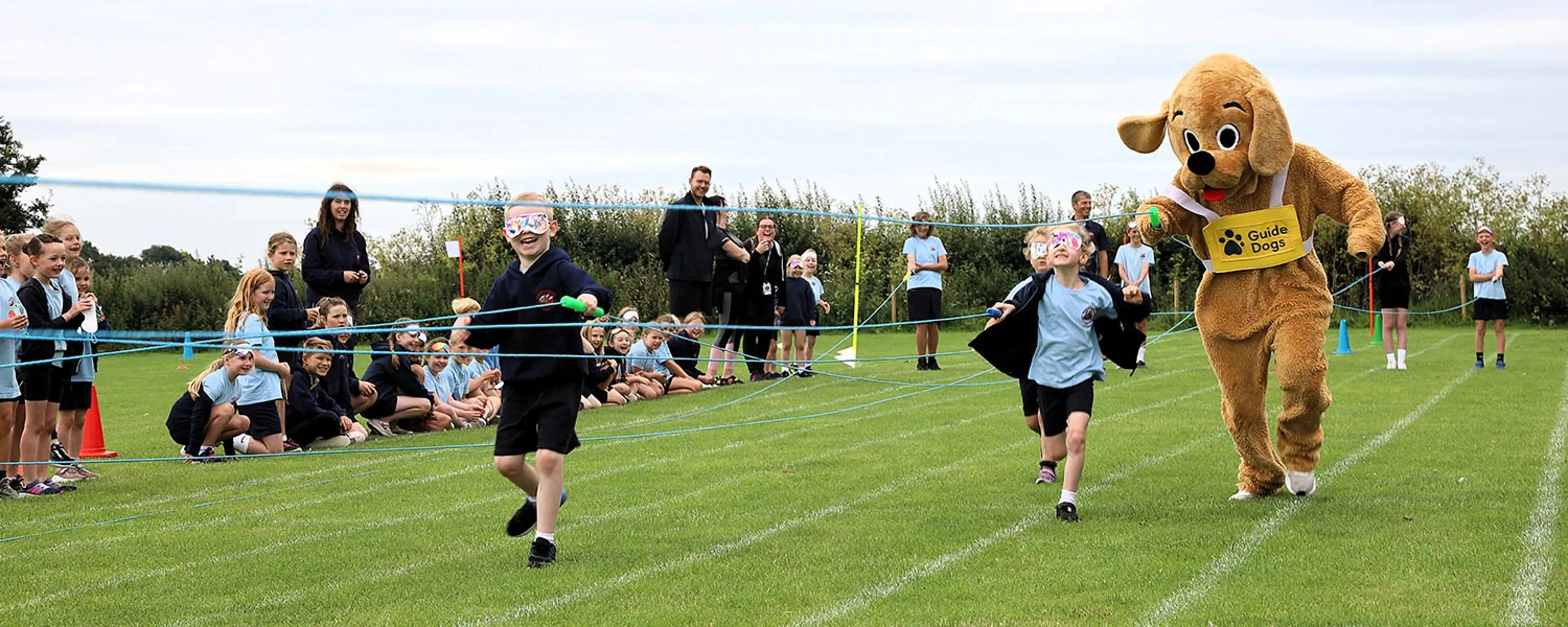 A school's sports day with children running an inclusive race with ropes to hold whilst blindfolded. 