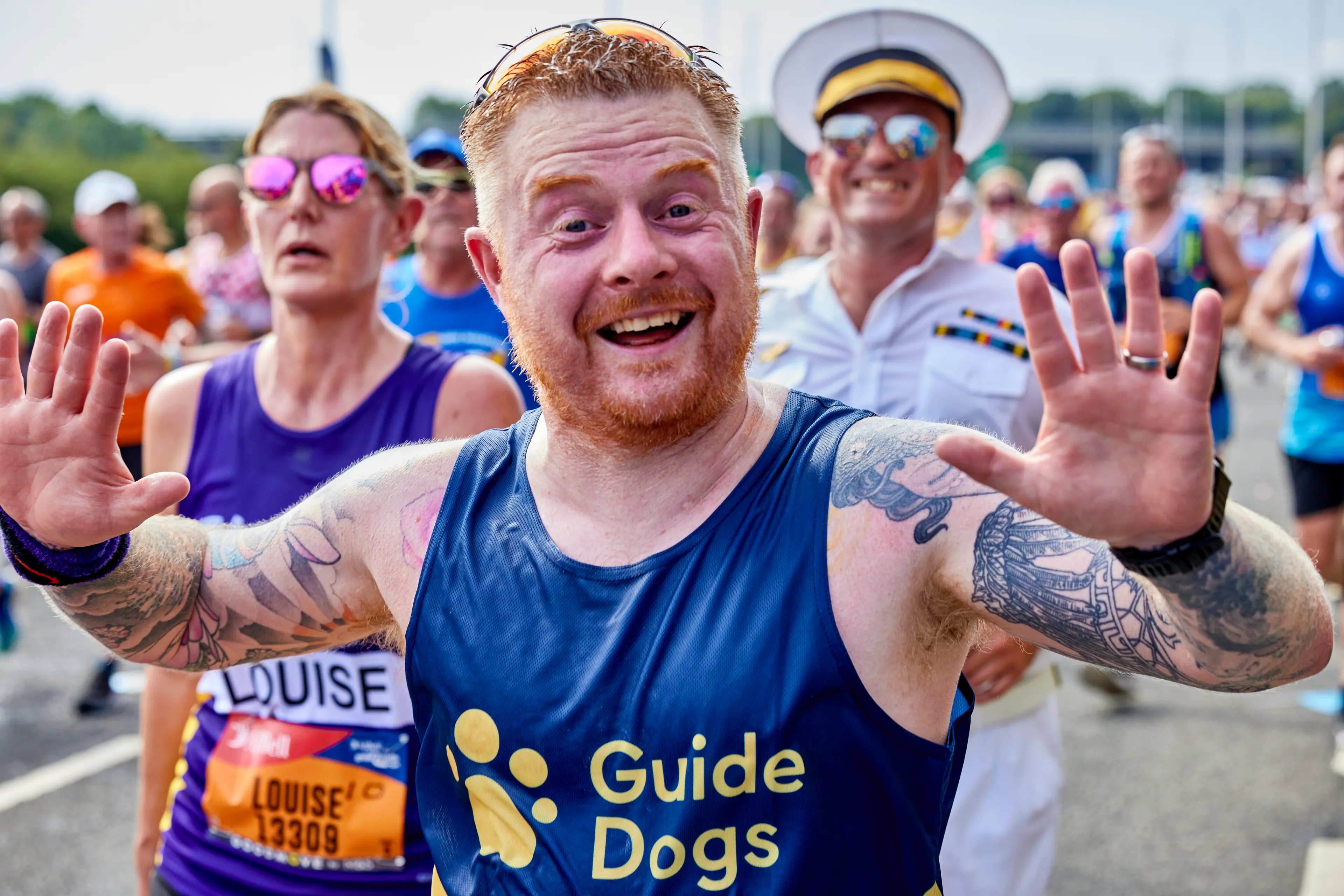 A runner for Guide Dogs waves his hand in the air as he passes cheering supporters.