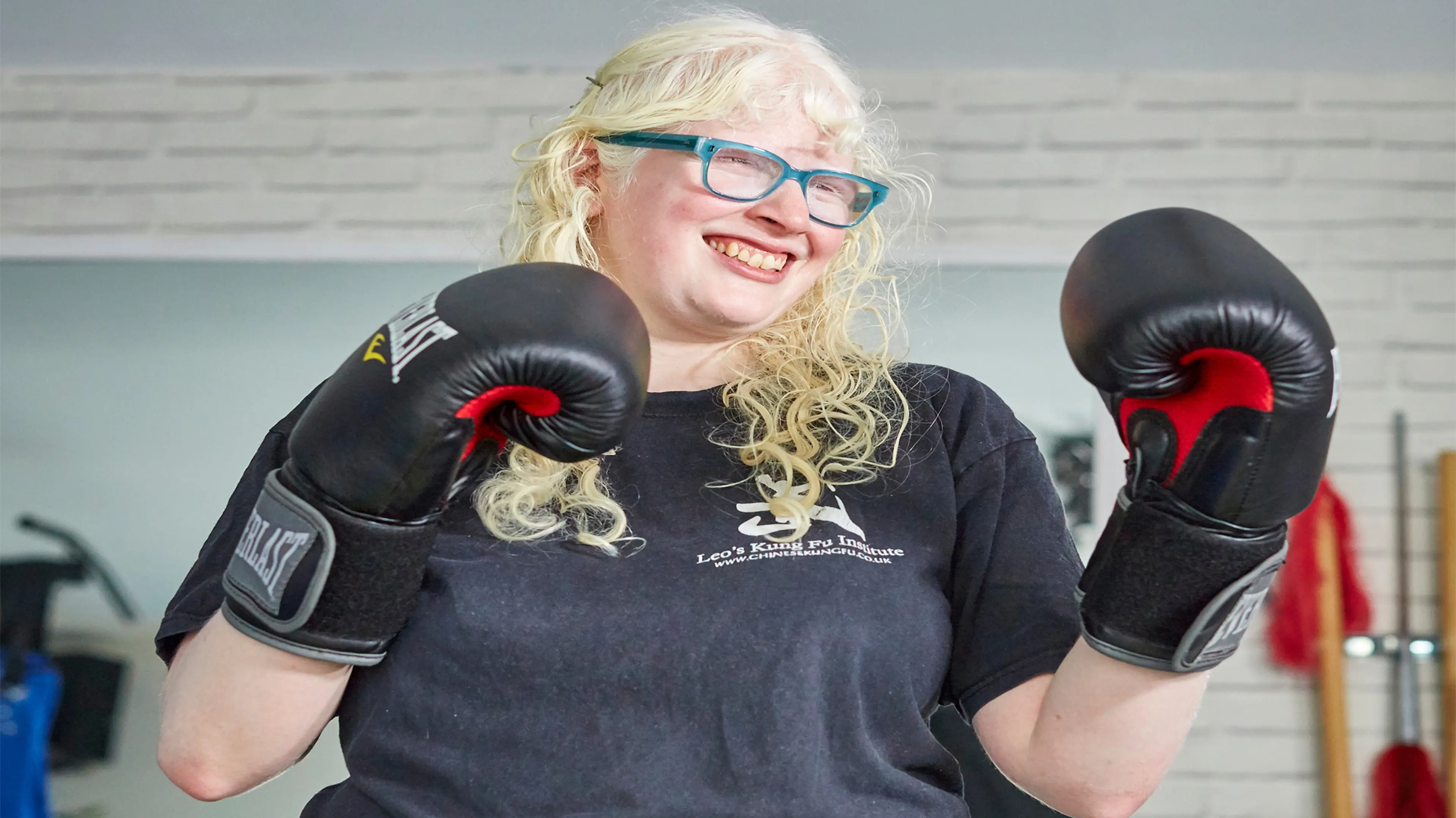 Guide dog owner Karishma smiles as she stands in a boxing stance with her boxing gloves on.