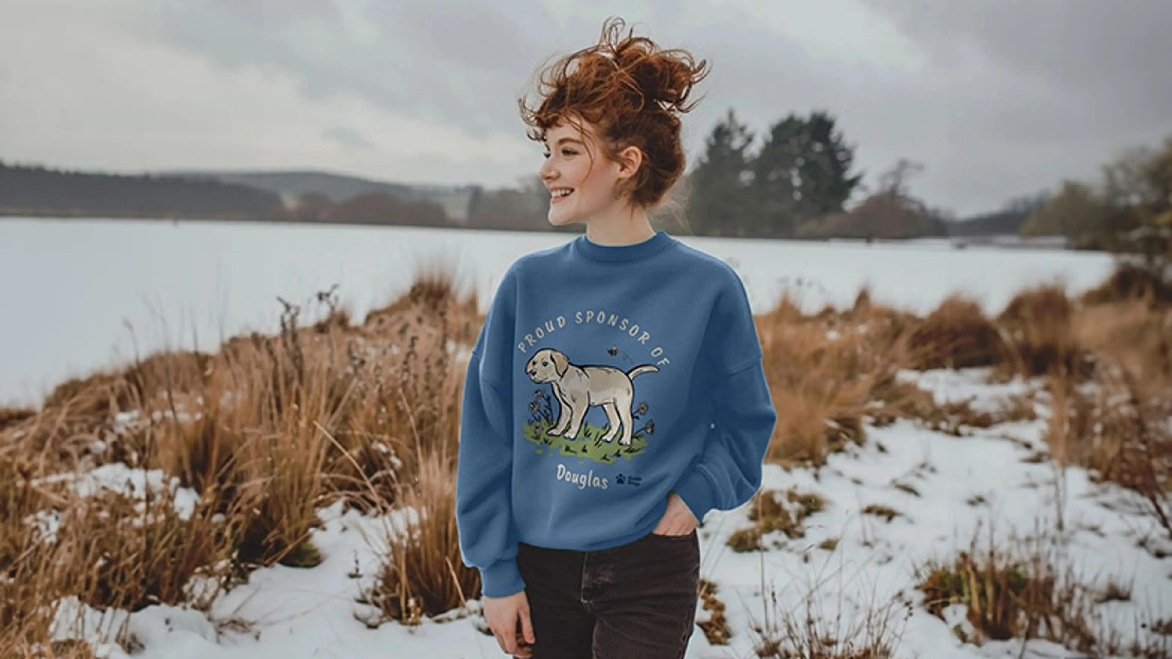 A woman in the snow covered countryside wearing a sweatshirt with sponsored pup Douglas design.