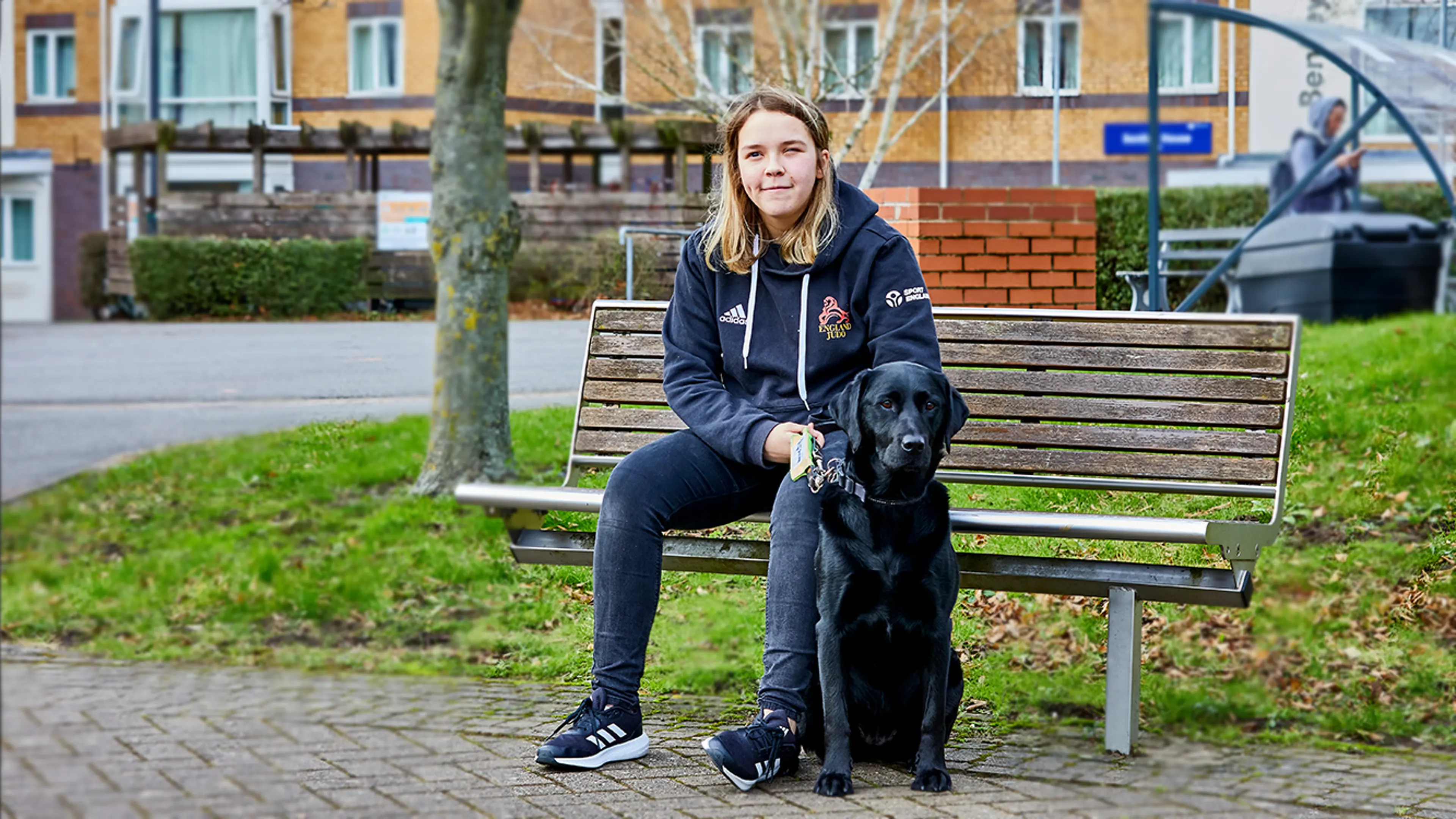 Caitlin, sitting on a bench with Honey, her guide dog.