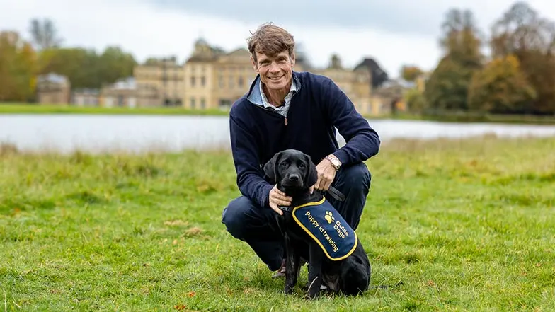 William Fox Pitt, Olympic Event Rider, posing in front of Badminton House with a black labrador puppy in training.