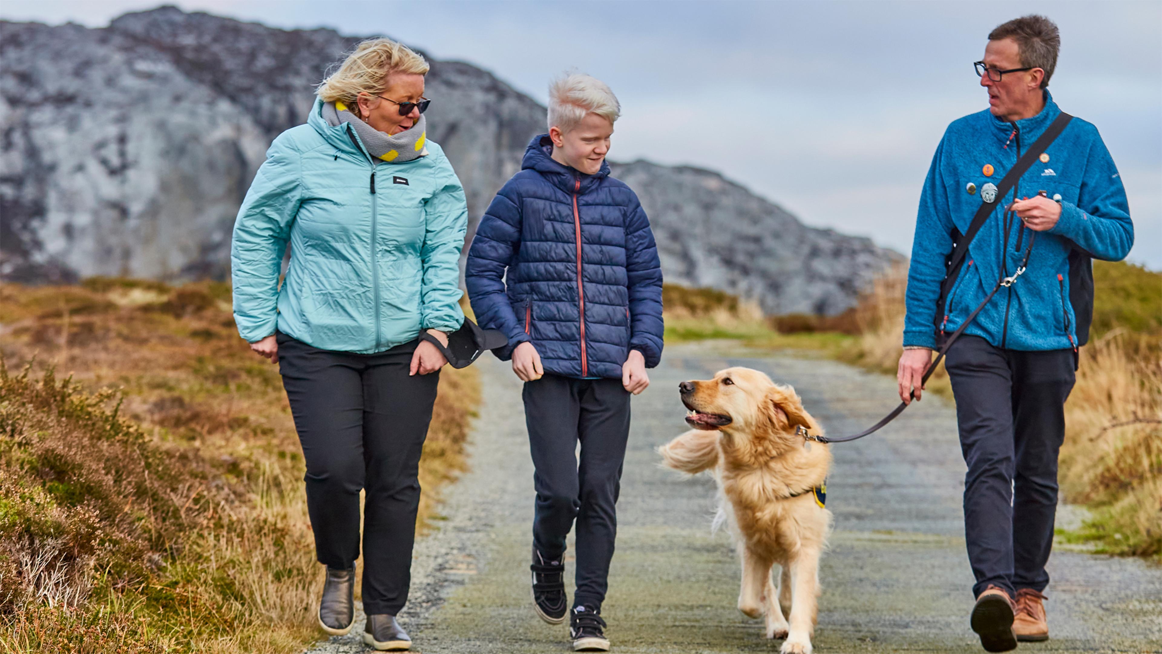 Ellis, who has a vision impairment, walks with his mum, dad and buddy dog Ralph down a path.
