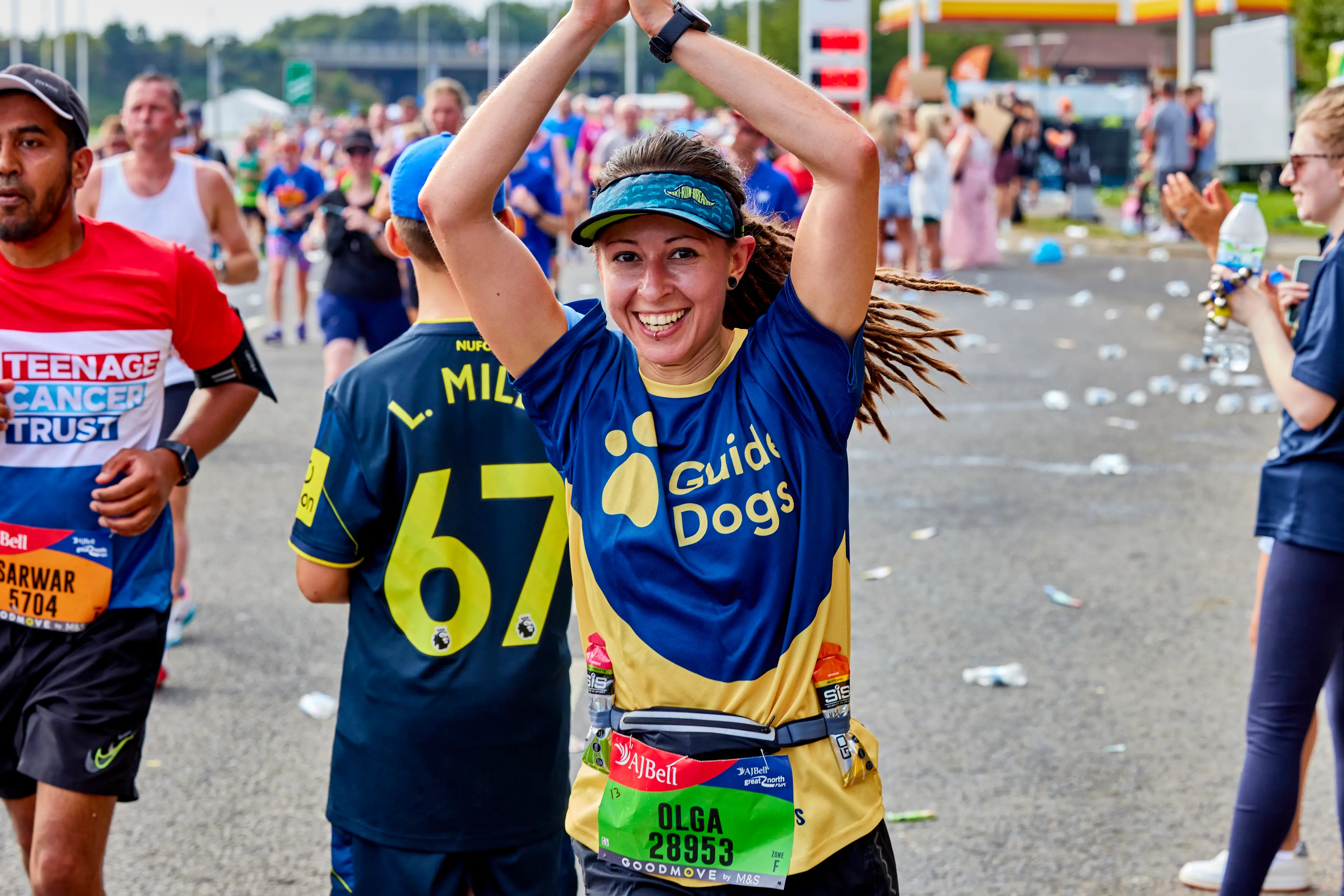 A runner for Guide Dogs waves her hands in the air as he passes cheering supporters.