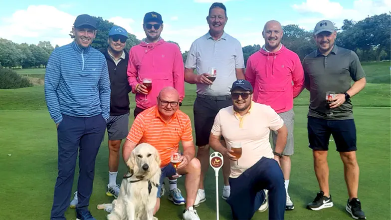A group of golfers on a golf course with a guide dog in training.