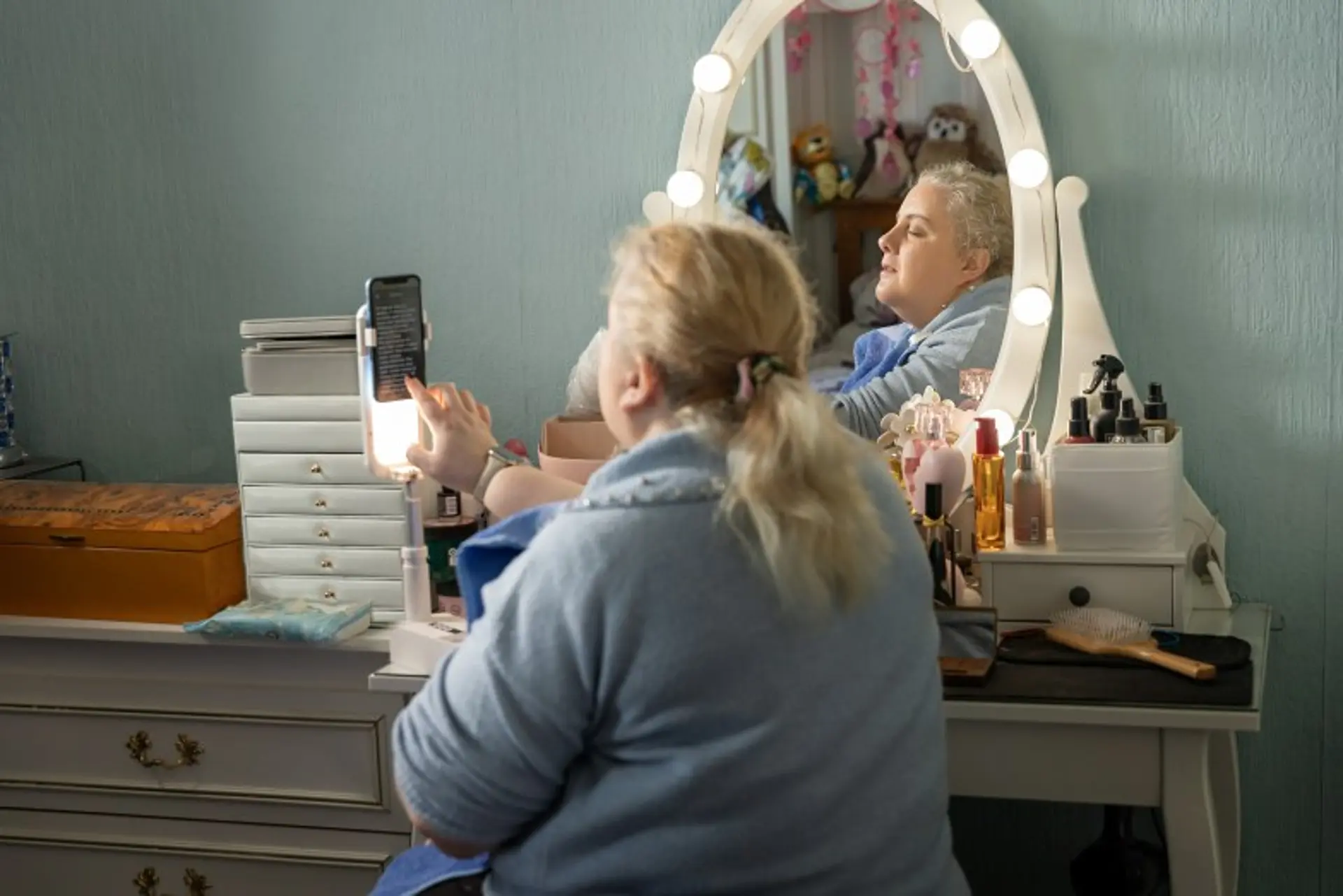 Marie uses an app on her phone to check her makeup while sitting at her dressing table. 