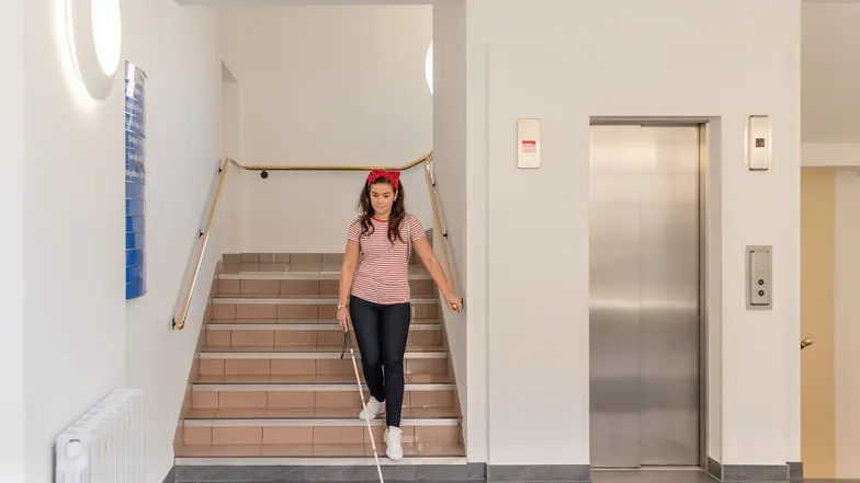 A woman using her long cane to travel down stairs.