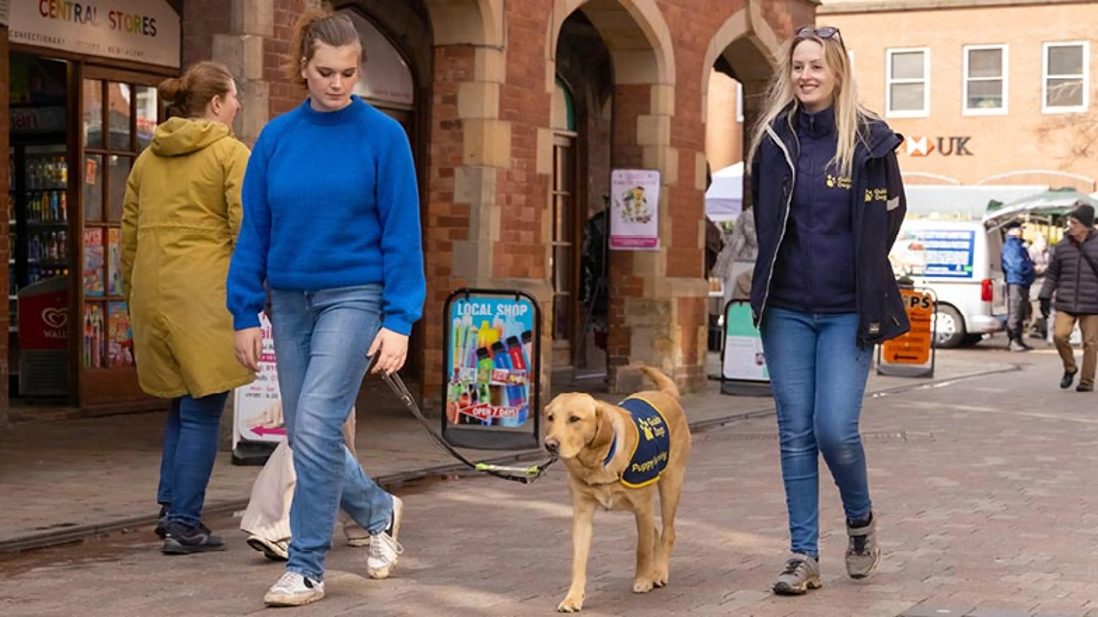 Puppy Raiser Ellen and Puppy Development Advisor Nichola walking with Buttons in a pedestrianised area.